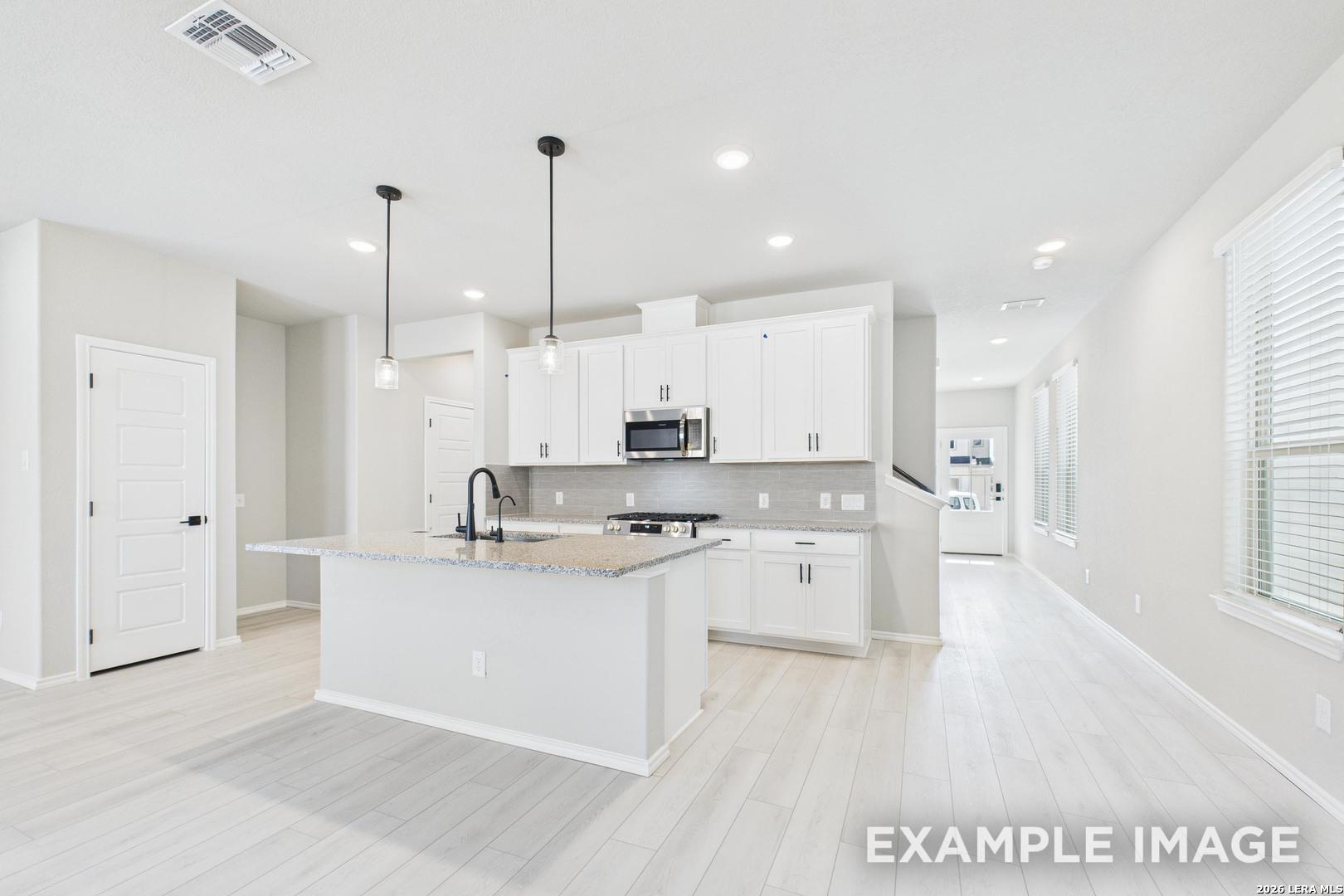Modern white kitchen with island, granite countertops, and pendant lighting in The Charlotte B plan at Cedar Heights, TX.