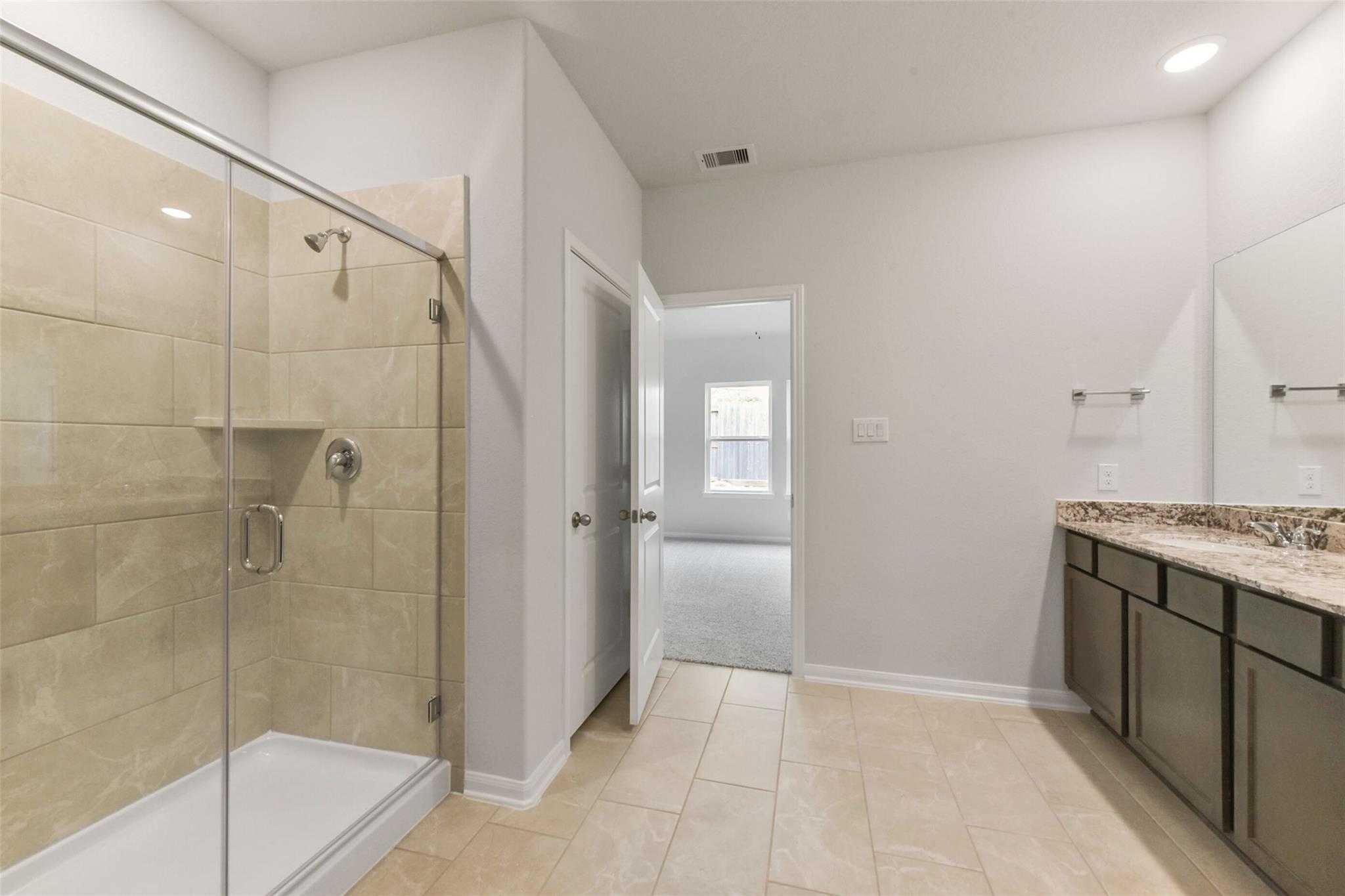 Modern master bathroom with glass walk-in shower, double vanity, and beige tile in Davidson Homes The Laguna B, Magnolia, Texas