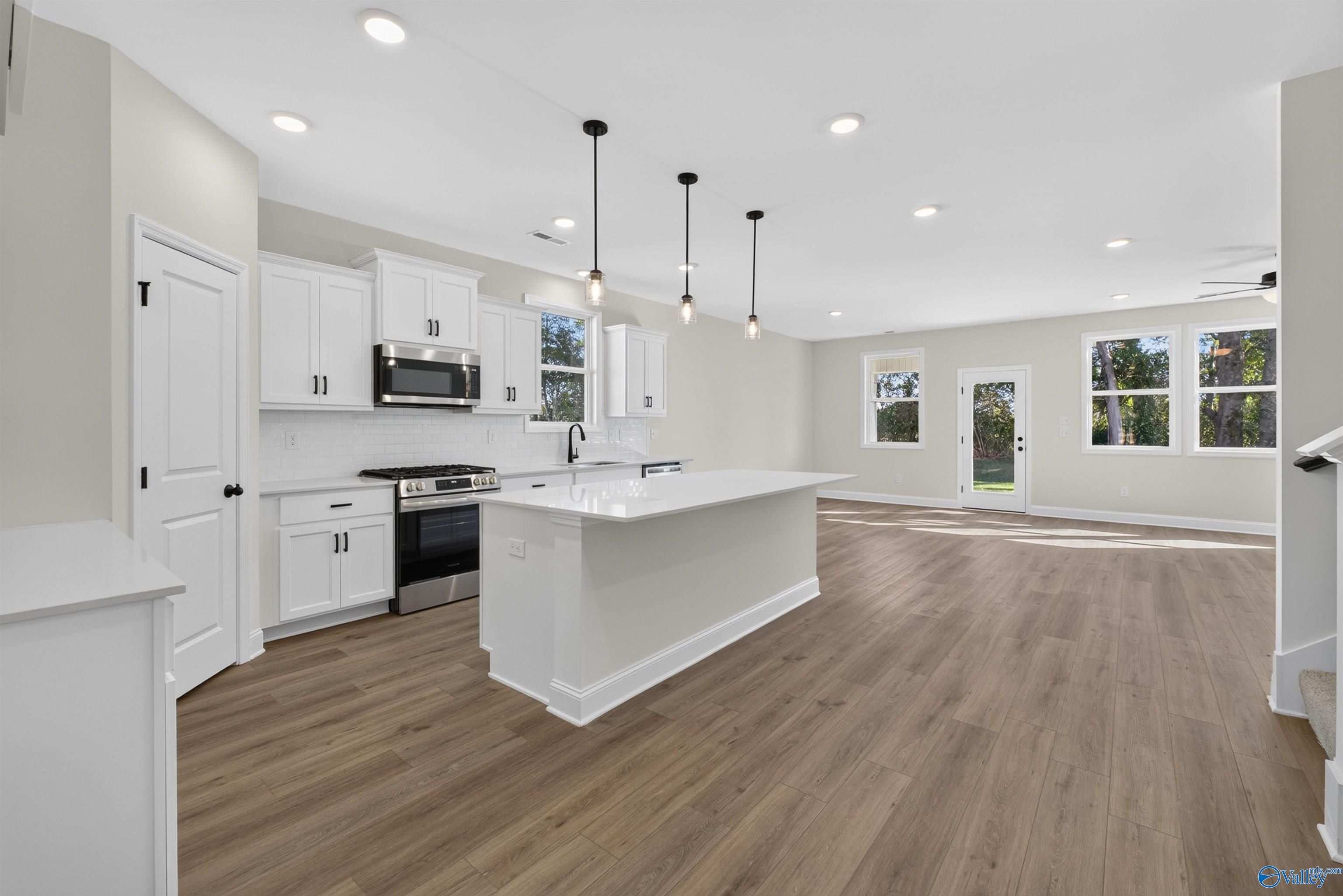 Open-concept kitchen with white shaker cabinets, center island, and luxury vinyl plank flooring in The Ashport L, Berry Cove, Alabama