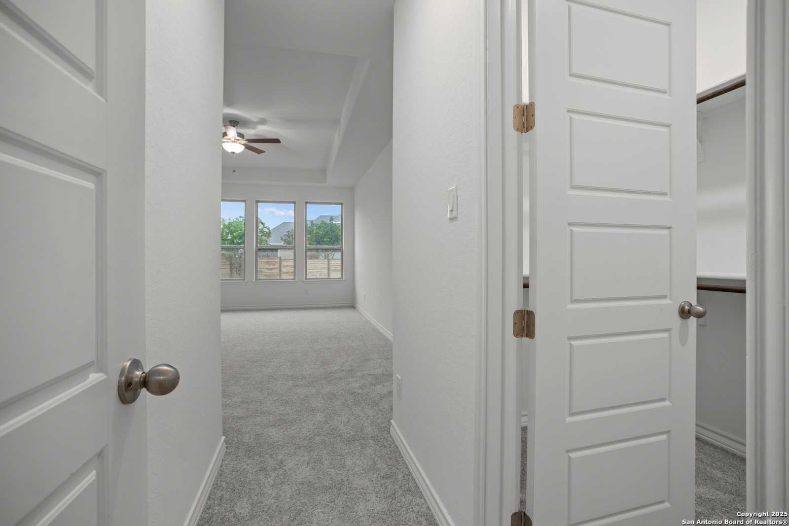 Spacious master bedroom with ceiling fan, large windows, and open walk-in closets in The Summerlin B, Castroville, Texas