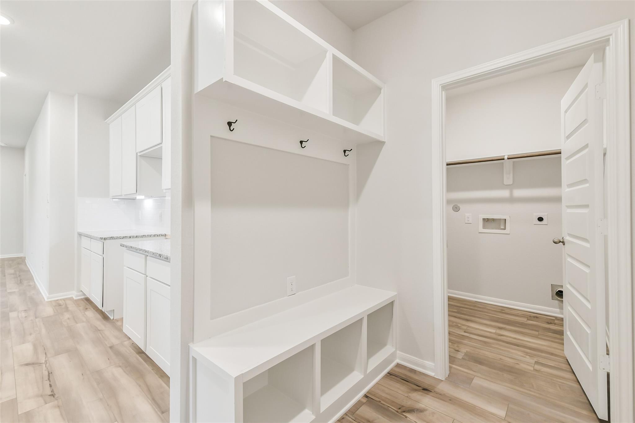 White mudroom with built-in bench, coat hooks, cubbies, and adjacent laundry in Davidson Homes The Brazos F, Conroe, TX