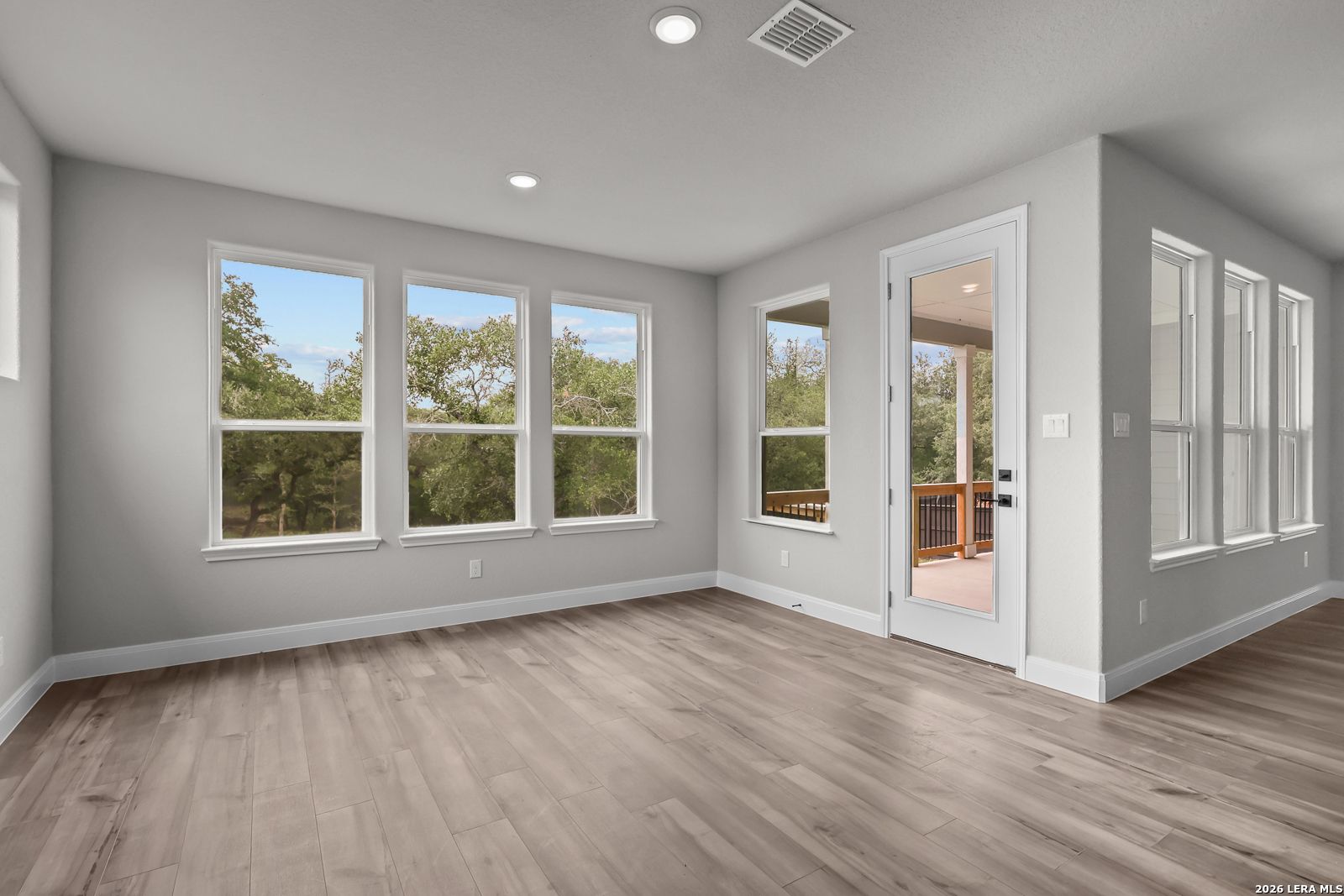 Bright upstairs bonus room with hardwood floors, gray walls, large windows to trees, and balcony door in The Belmont H, Castroville, Texas