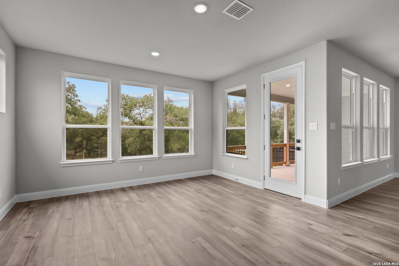 Bright upstairs bonus room with hardwood floors, gray walls, large windows to trees, and balcony door in The Belmont H, Castroville, Texas