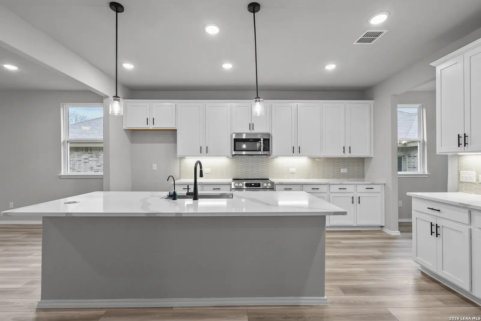 Modern kitchen with white cabinets, quartz island, and pendant lighting in Davidson Homes' The Glenwood E, San Antonio.