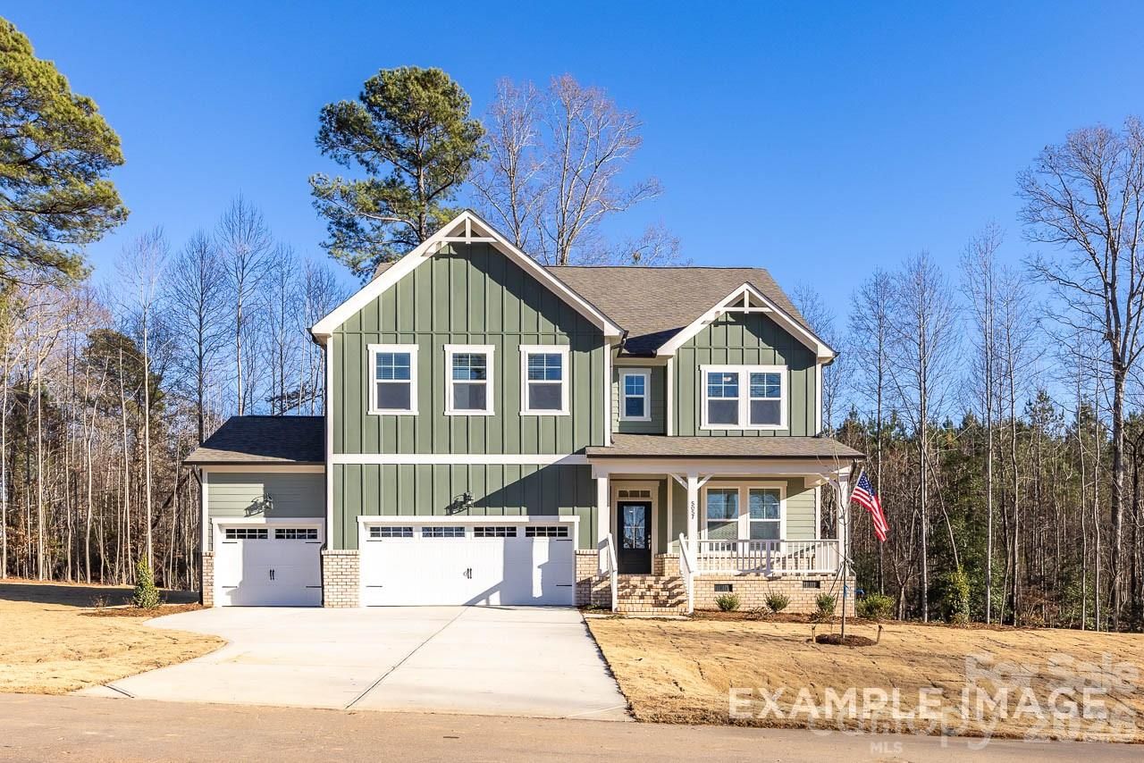 Two-story green Davidson Homes Aspen B with covered front porch, 3-car garage, and American flag in Windgate, Mooresville, NC
