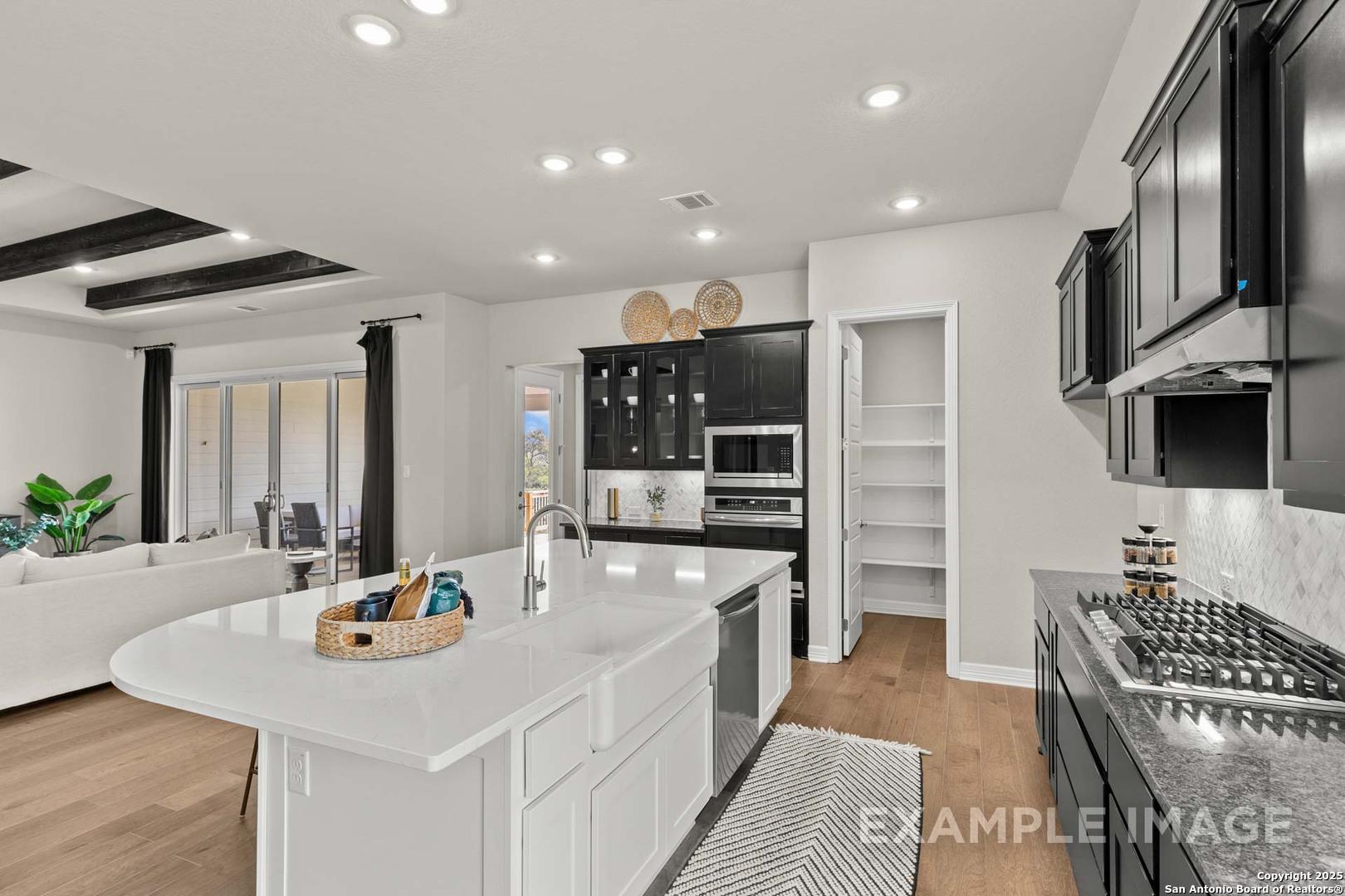 Modern kitchen featuring white quartz island, farmhouse sink, black cabinets, and stainless appliances in Davidson Homes Summerlin B, Castroville, TX