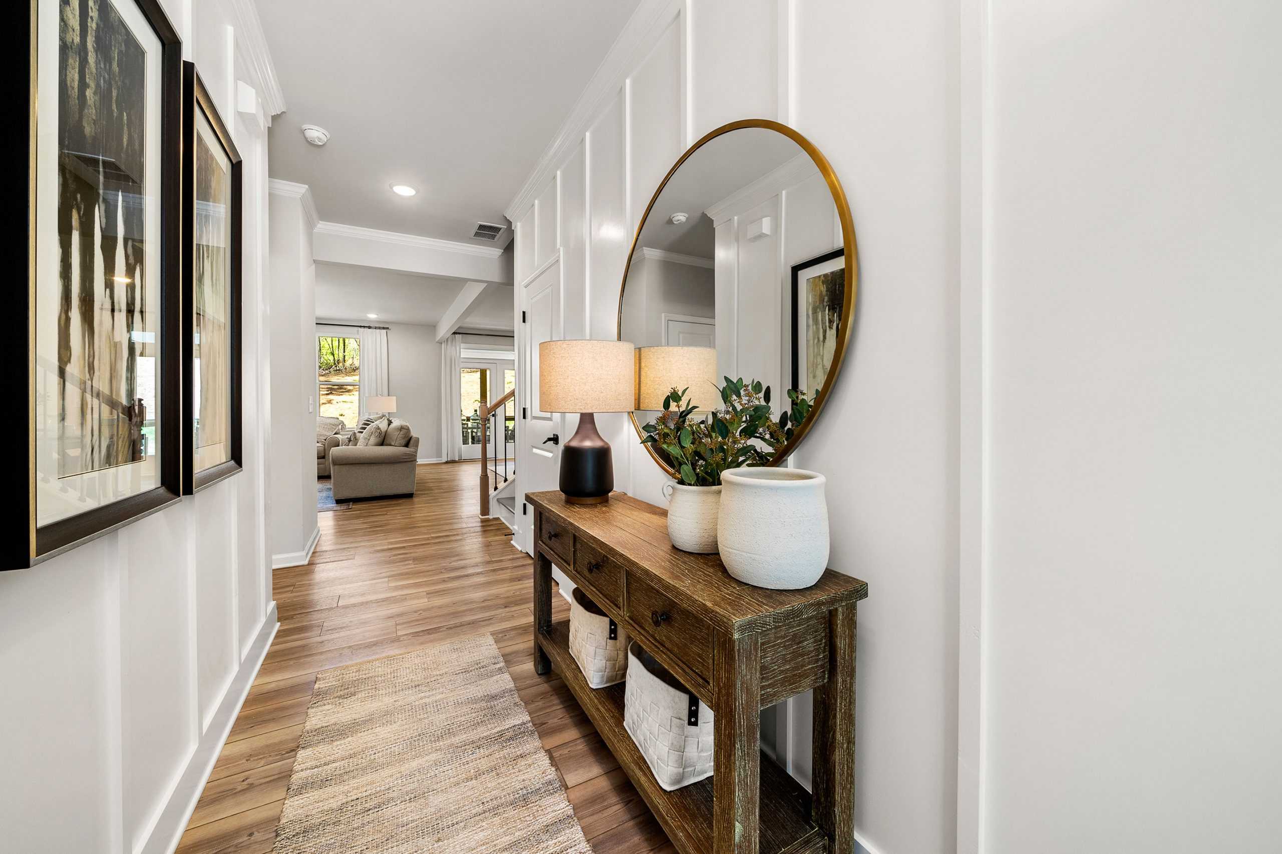 Elegant foyer hallway at Riverwood in Dallas Georgia with white shiplap walls, gold round mirror, wooden console table, lamps and plants