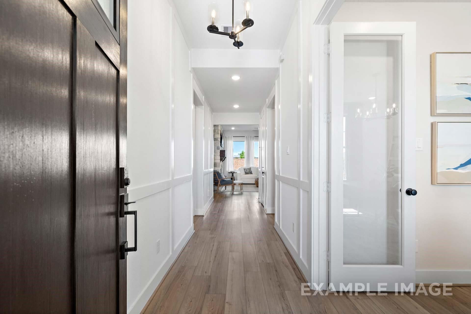 Bright entry hallway with dark wood door, hardwood floors, wainscoting, and chandelier in Davidson Homes The Edward A, Lago Mar