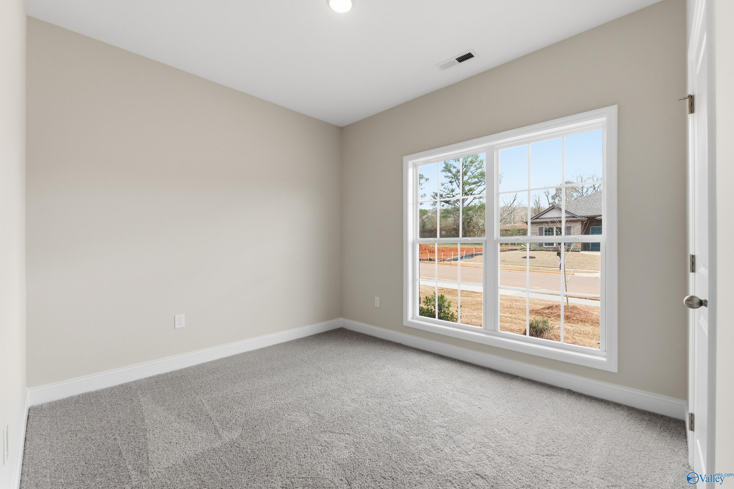 Bright bedroom with beige walls, gray carpet, and large window overlooking backyard in The Asheville C, Jaguar Hills, Huntsville, AL