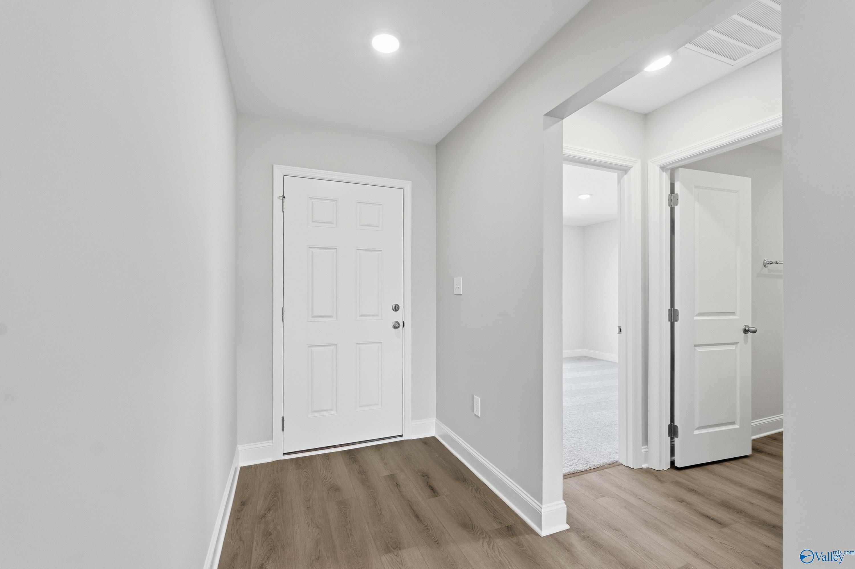 Bright hallway featuring white doors, gray walls, and wood flooring in Davidson Homes The Franklin, New Market, Alabama