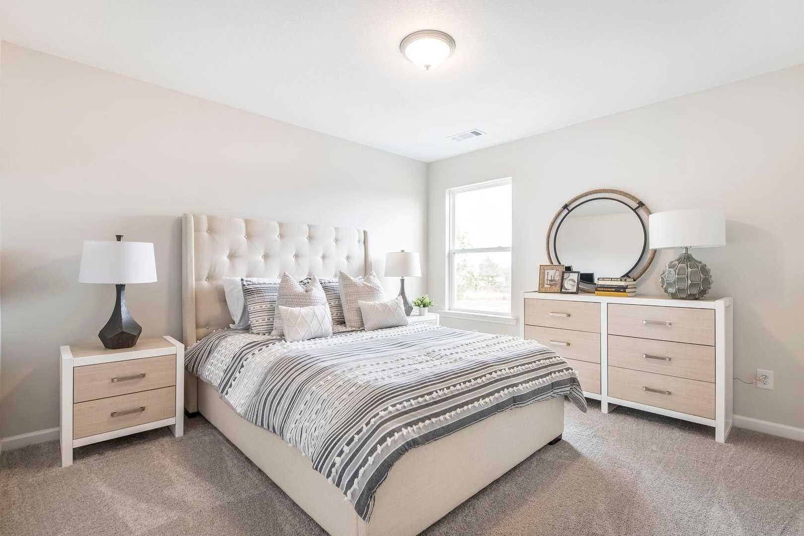 Spacious primary bedroom at Cape Reserve Donahue Ridge in Auburn Alabama with king bed tufted headboard striped bedding and beige walls