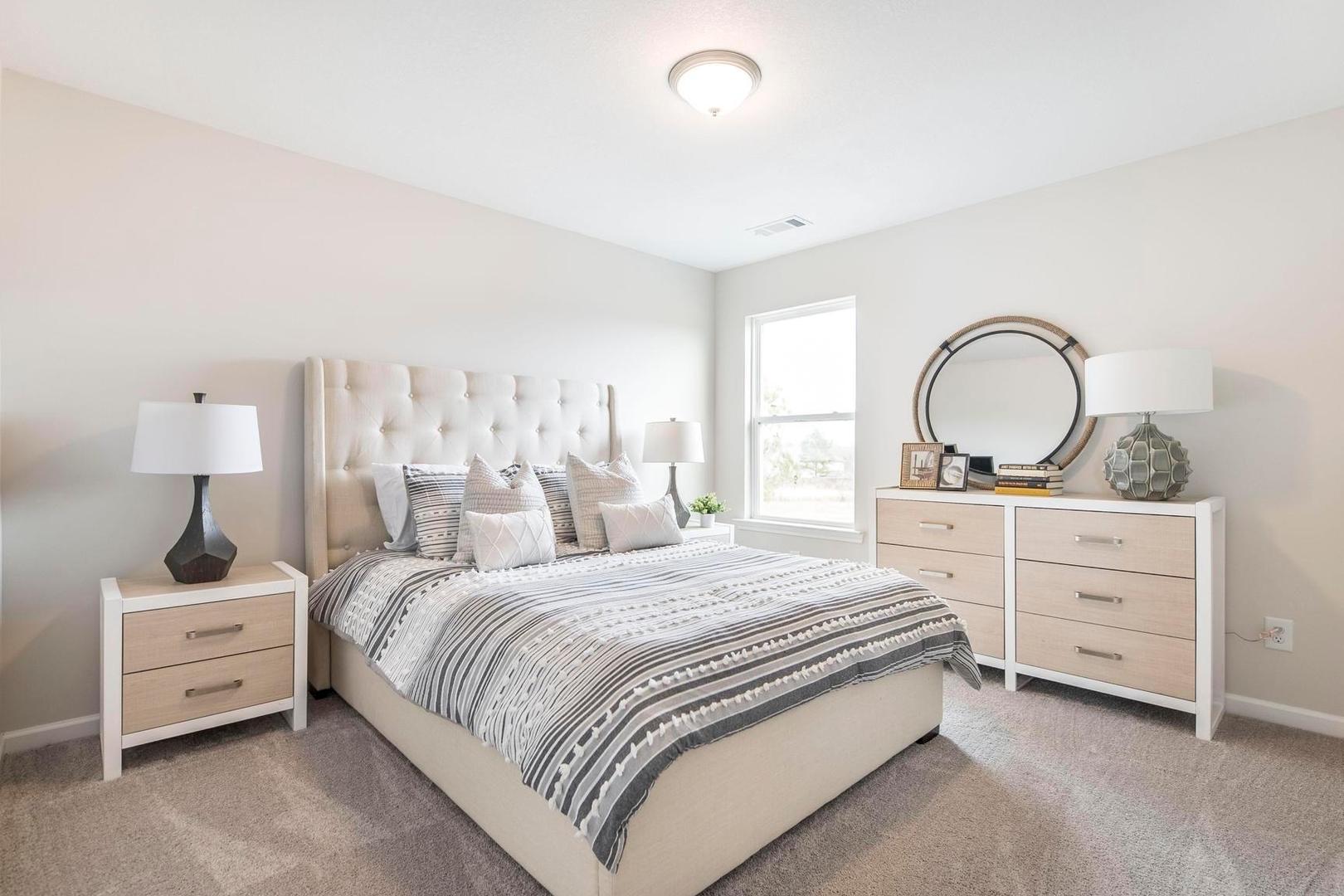 Spacious primary bedroom at Cape Reserve Donahue Ridge in Auburn Alabama with king bed tufted headboard striped bedding and beige walls
