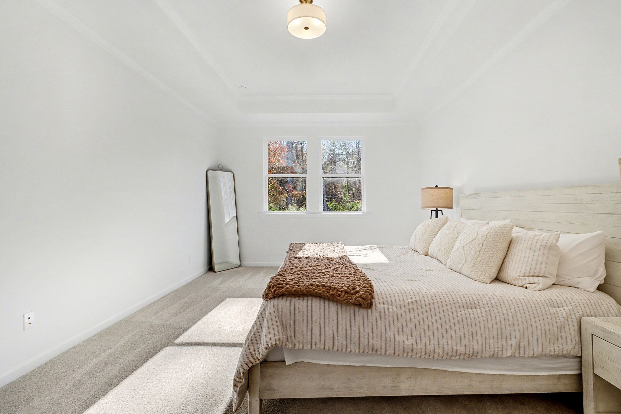 Elegant master bedroom with king bed, tray ceiling, large windows, and neutral tones in Davidson Homes The Daphne B, Loganville, GA