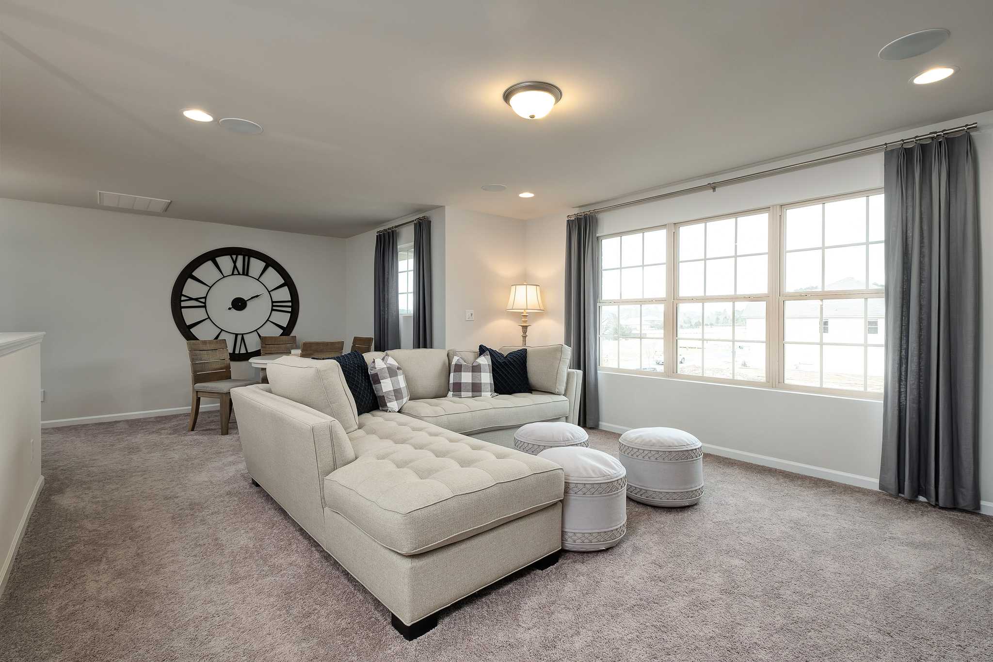 Cozy living room at The Reserve at Overton in Hampton Cove AL with beige sectional sofa, pillows, ottomans, wall clock and large windows