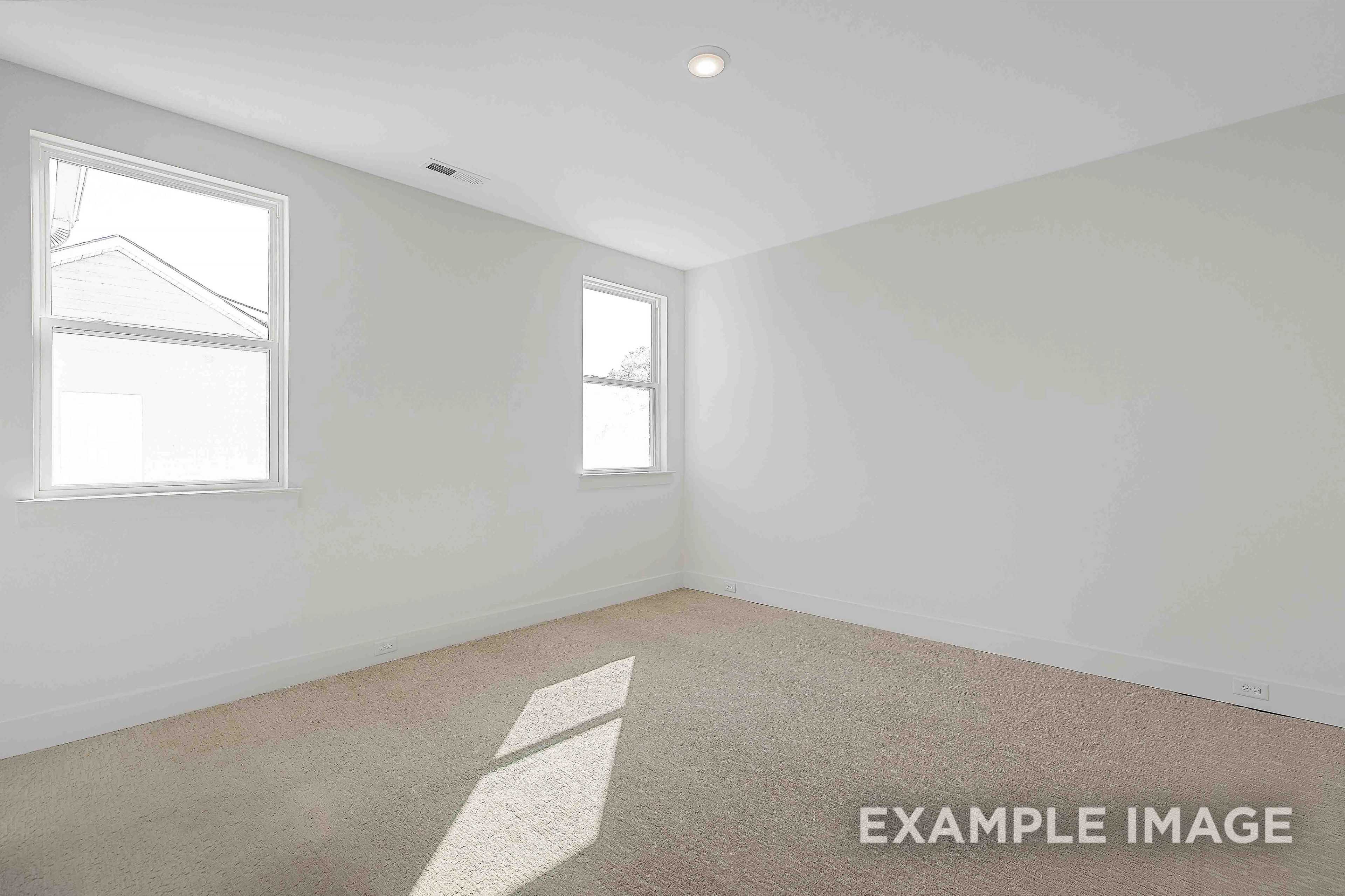 Spacious empty bedroom in The Albany A with white walls, beige carpet, and large windows streaming natural sunlight