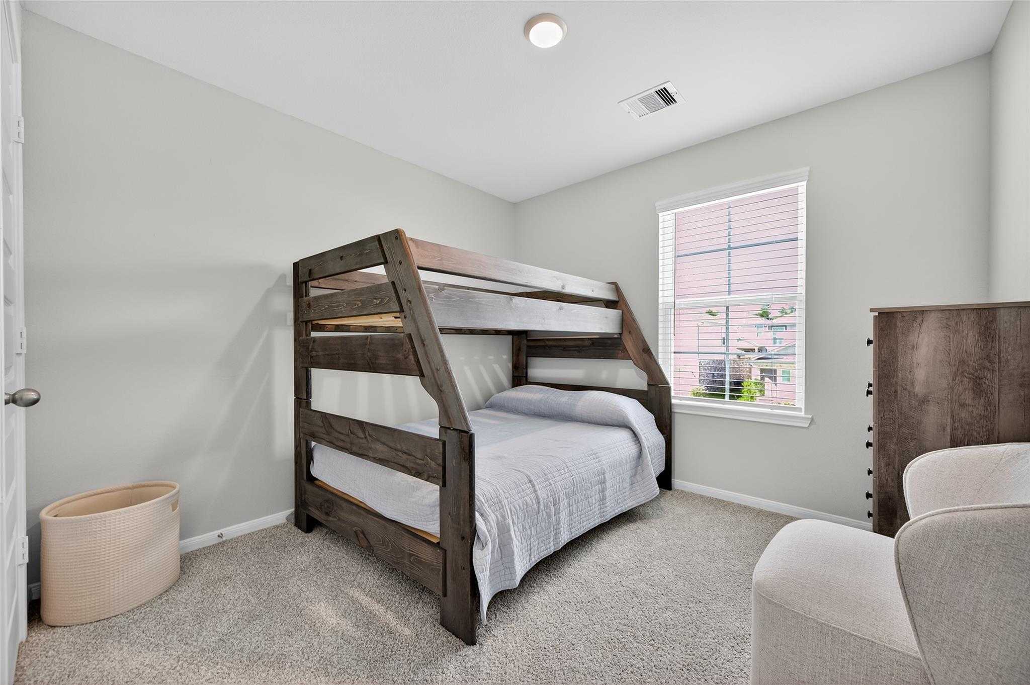 Rustic wooden bunk bed with bedding in cozy gray-walled bedroom, dresser, armchair in 5-bedroom Davidson Homes The Brazos E, Magnolia TX