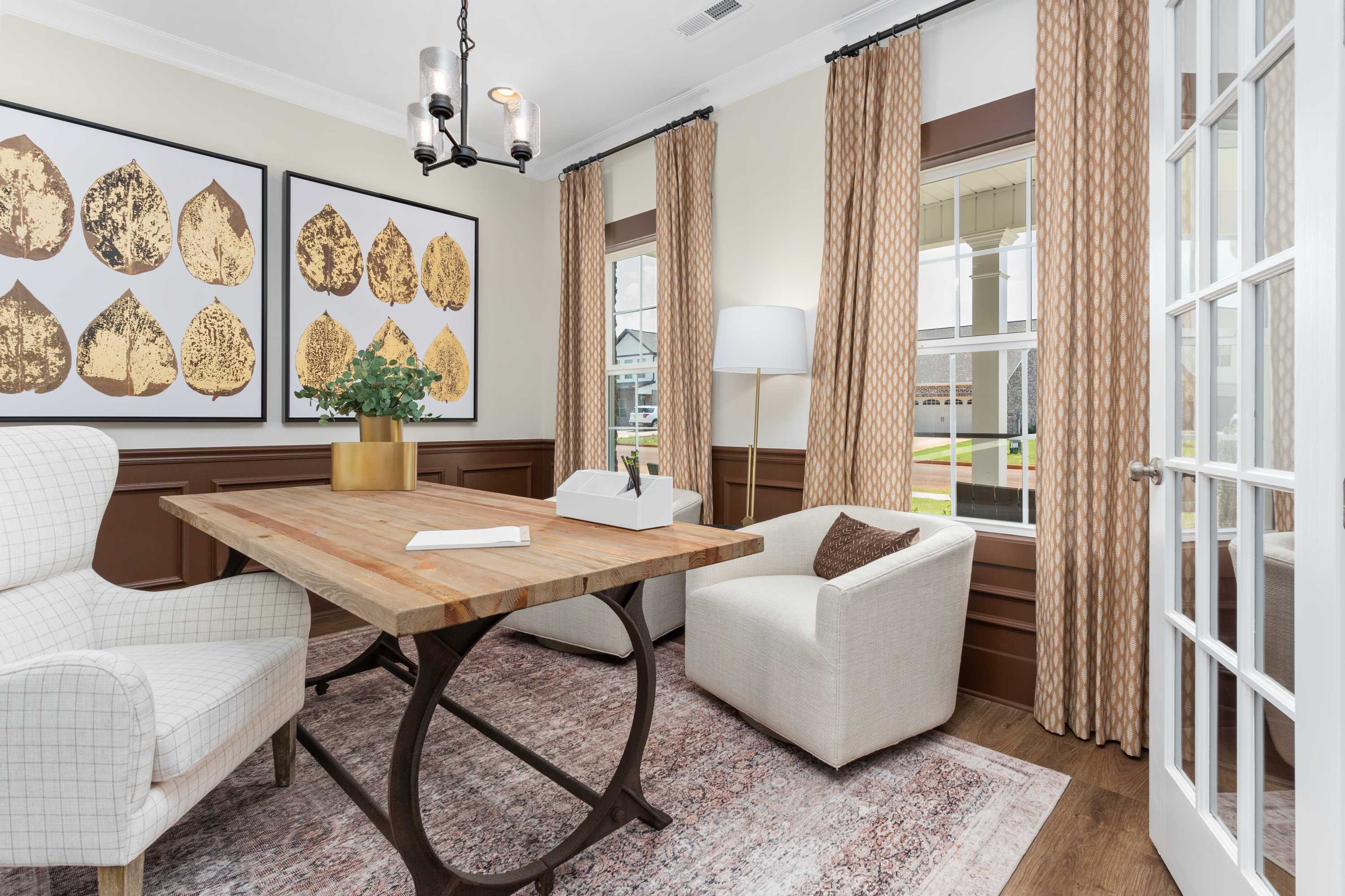 Cozy home office in The Shelby A with wooden desk, gold leaf wall art, chandelier, and French doors to yard