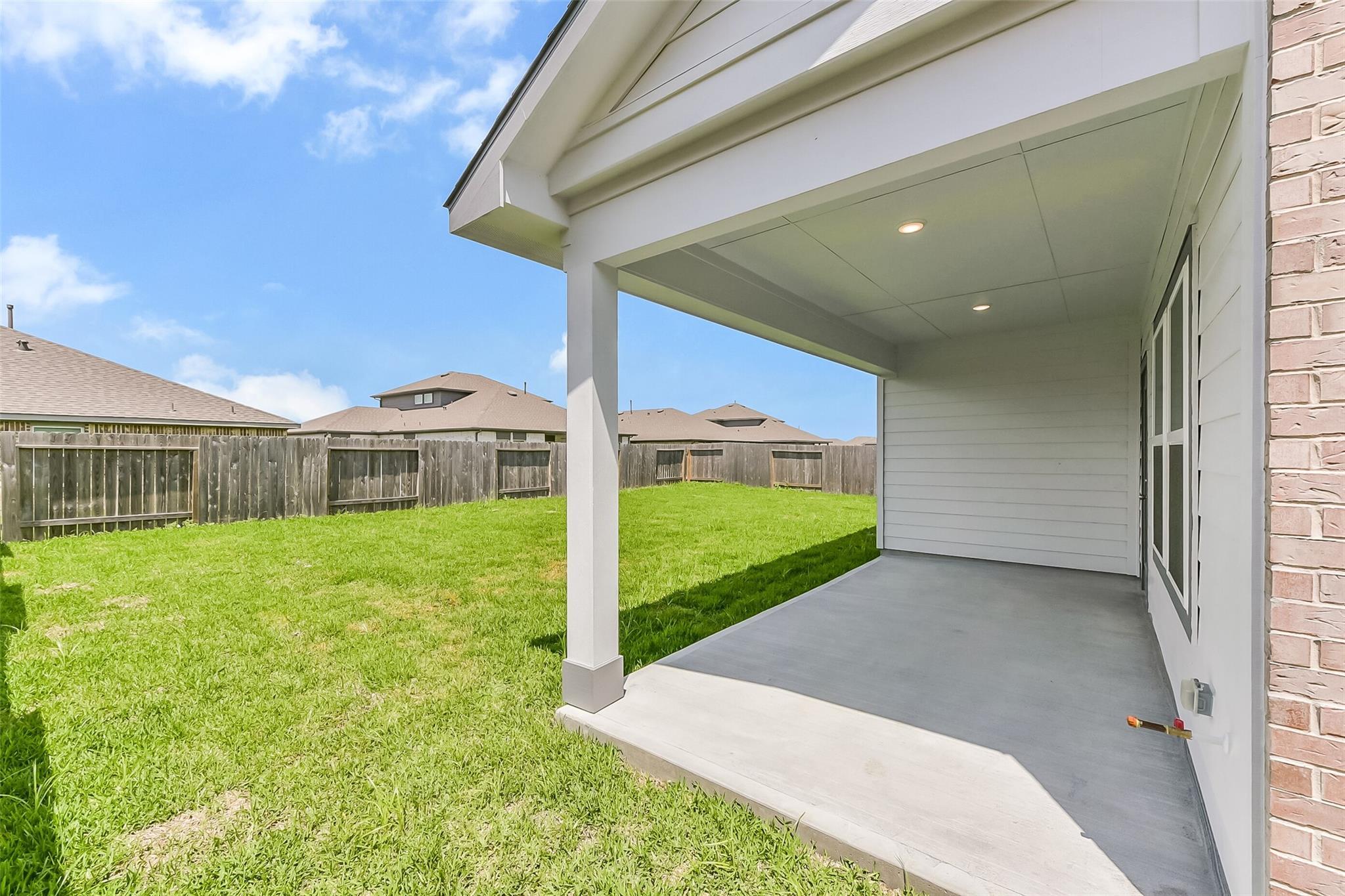 Covered patio with white columns and recessed lights overlooking lush green backyard in Davidson Homes The Tierra C, Dayton, Texas