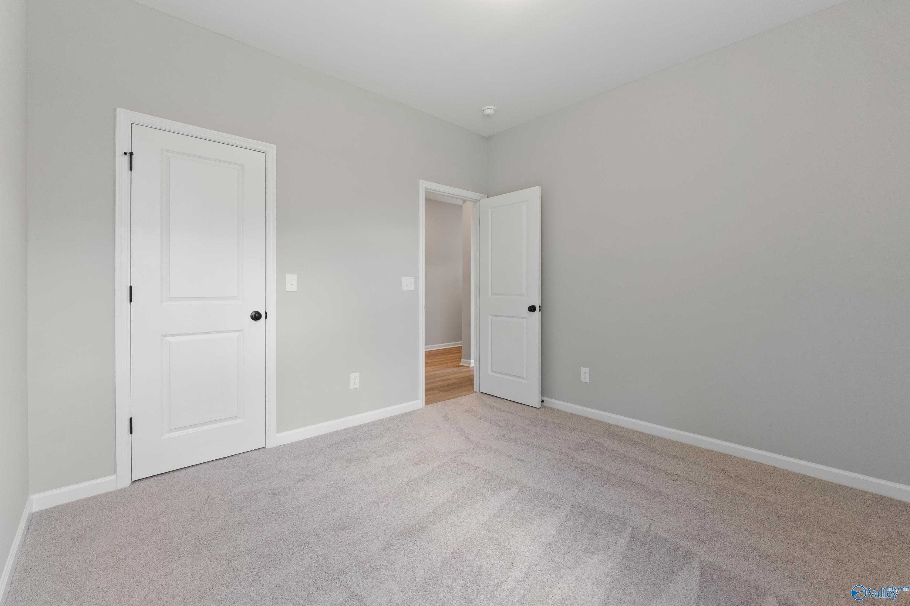 Spacious empty bedroom with light gray walls, beige carpet, and white doors in Davidson Homes The Phoenix, Hazel Green, AL