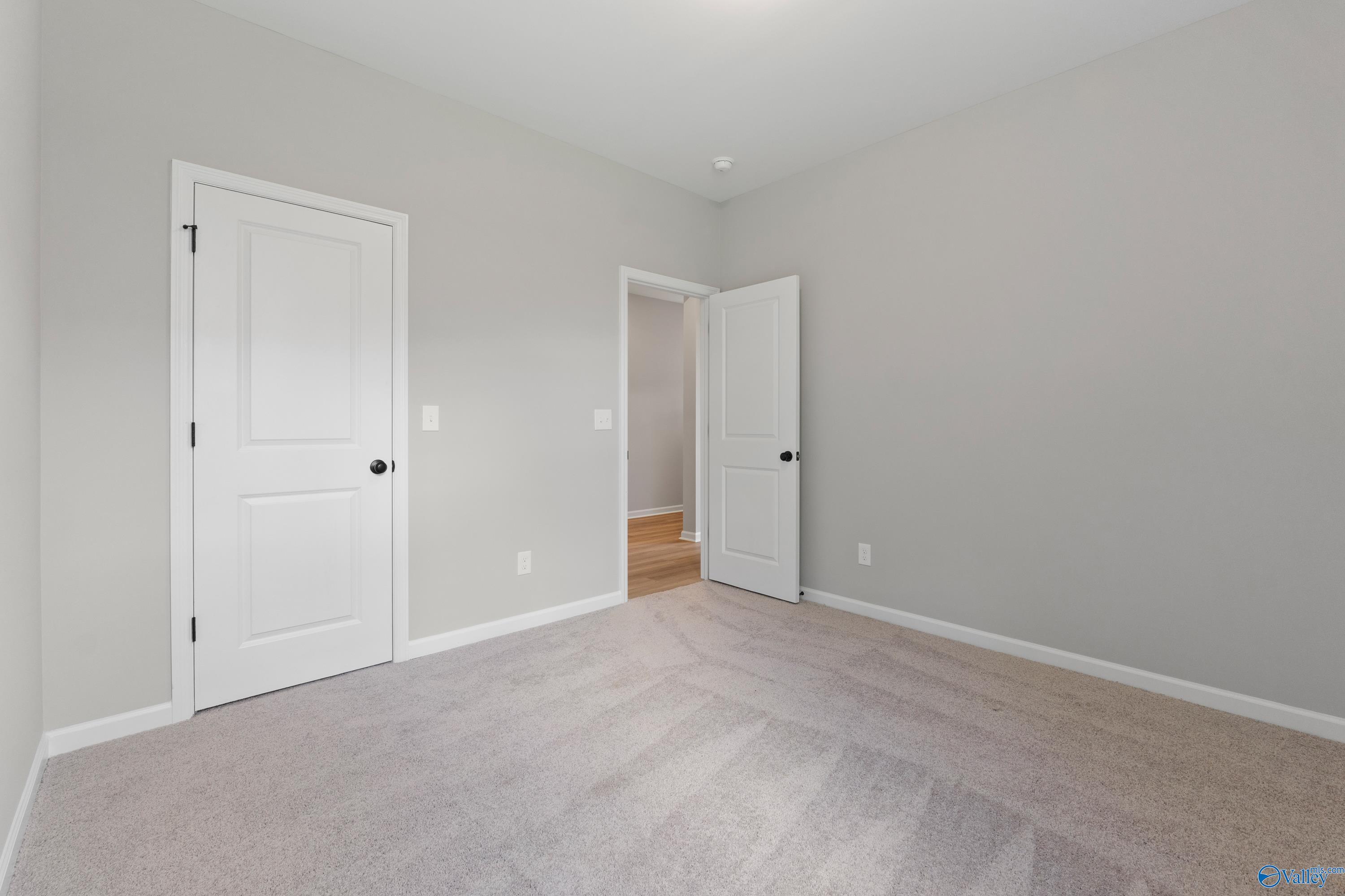 Bright secondary bedroom with light gray walls, beige carpet, and open doorway in Davidson Homes The Phoenix, Hazel Green, Alabama