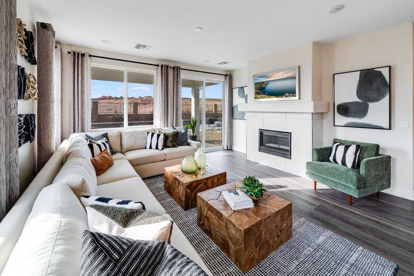 Spacious living room in The Boulder II: white L-shaped sofa, wooden coffee table, green accent chair, gas fireplace, large windows with desert view