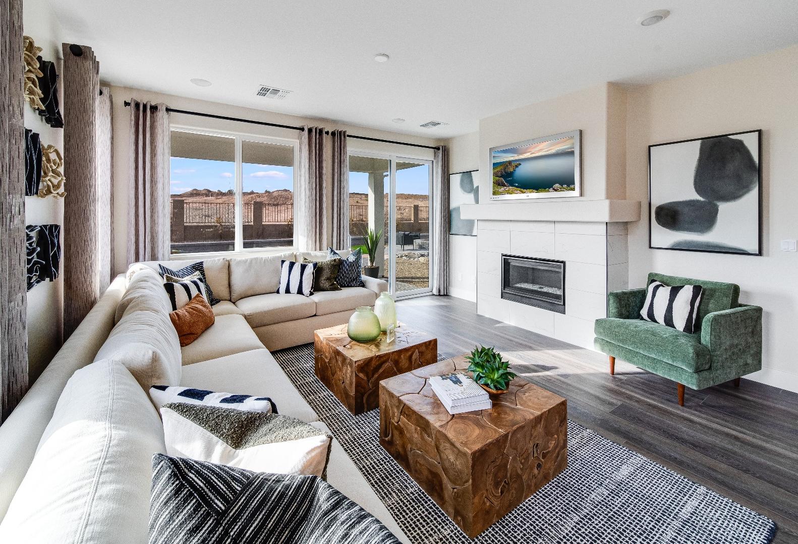 Spacious living room in The Boulder II with white L-shaped sofa, wooden coffee table, green accent chair, fireplace, and sliding doors to patio