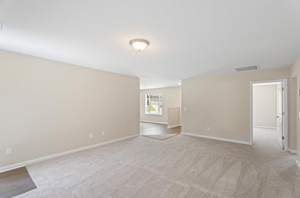 Spacious open living area with beige walls, carpet flooring, and adjacent doorways in Davidson Homes The Washington, Phenix City, Alabama