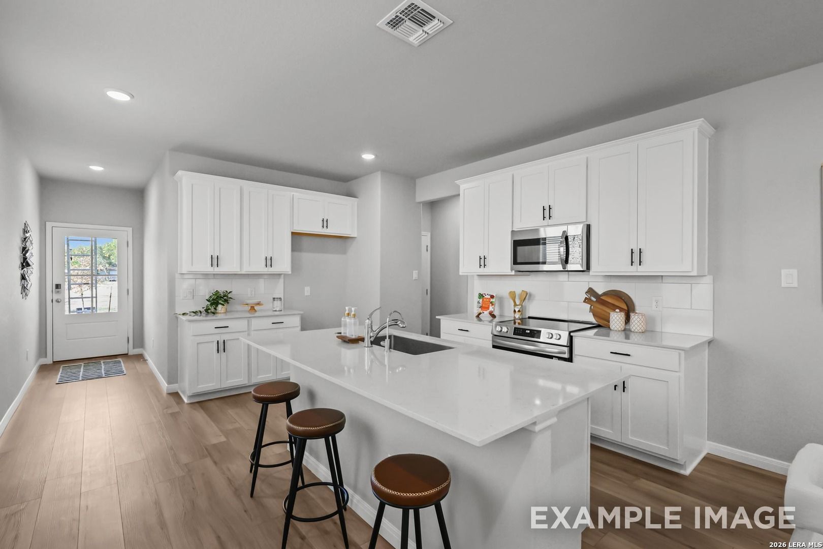 Modern kitchen with white cabinets, quartz island, and stainless appliances in The Gillian A, Cedar Heights, San Antonio.