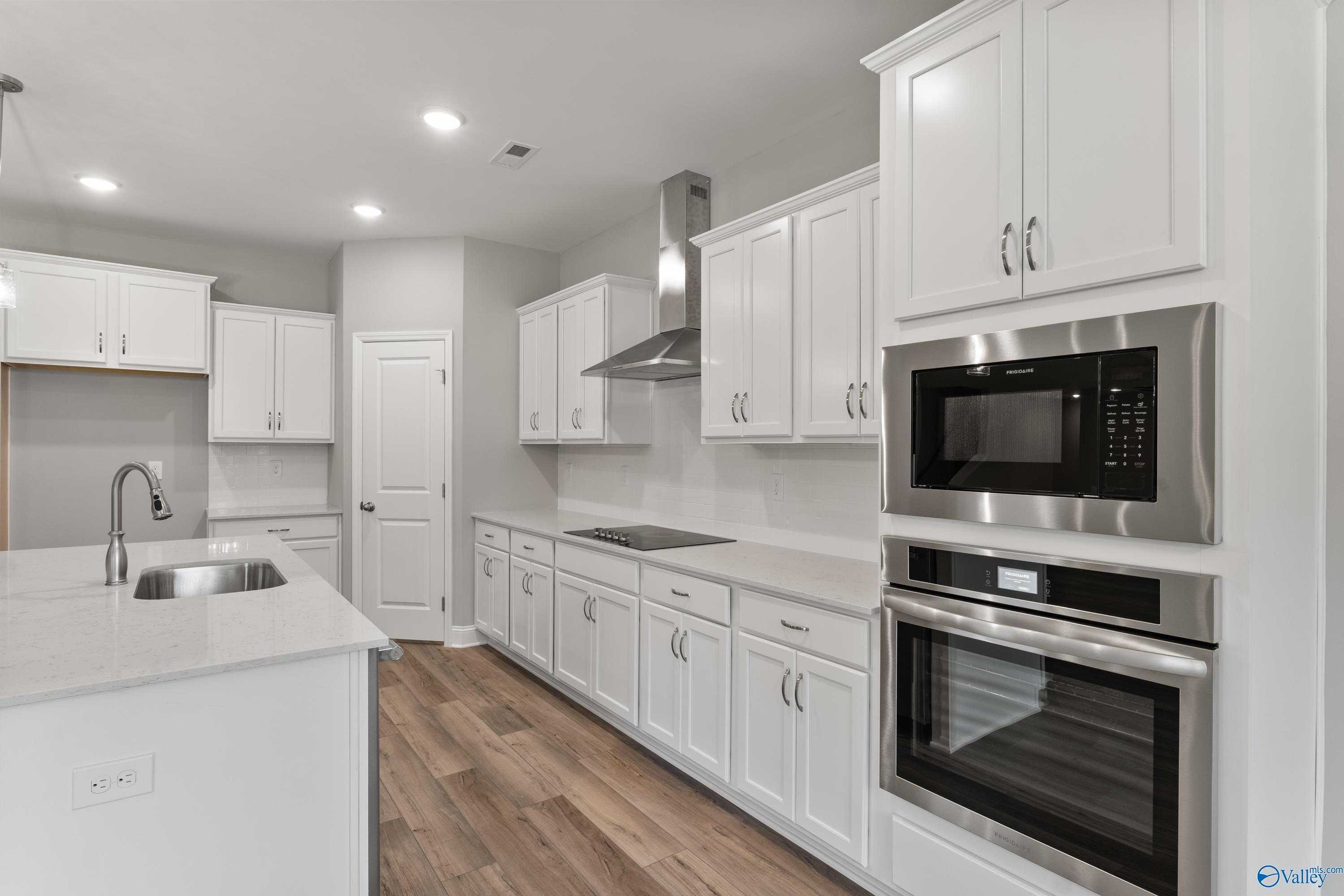 Modern white kitchen with shaker cabinets, quartz island, stainless appliances, and gas cooktop in Davidson Homes The Rockford, Harvest, AL