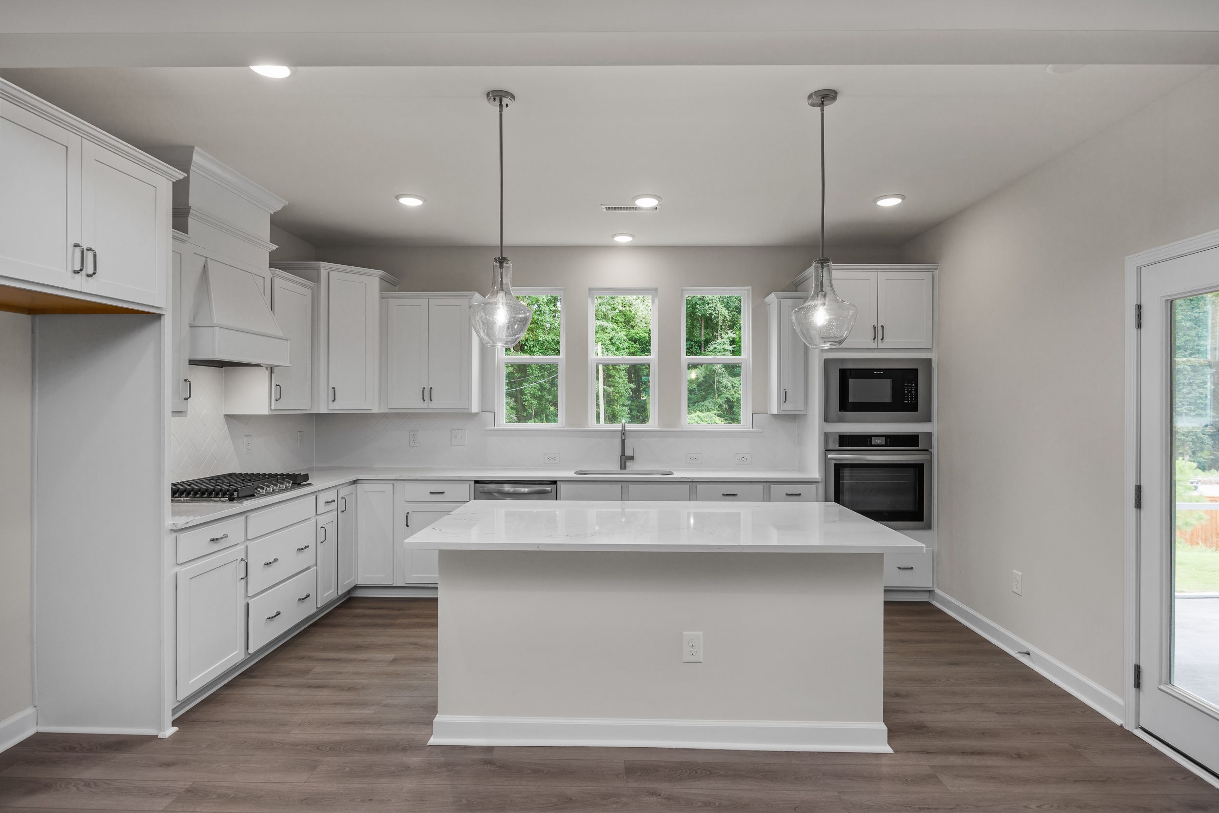 Modern white kitchen in The Aspen Davidson Homes with large quartz island, double ovens, and French doors to patio