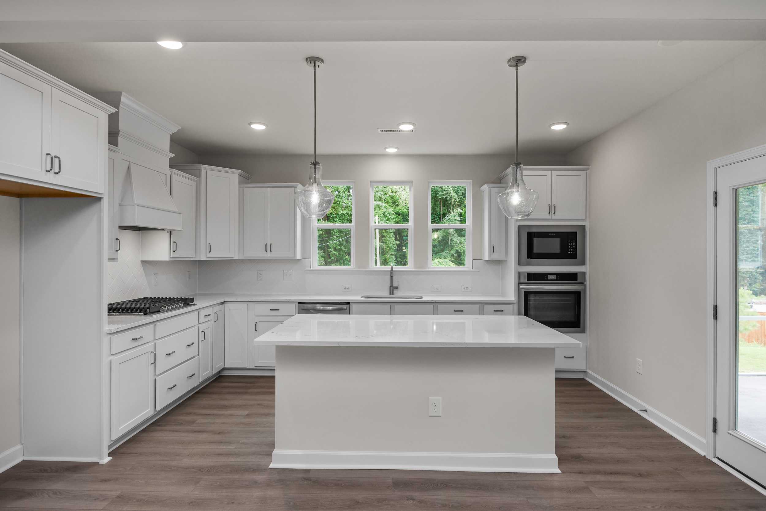Modern white kitchen in The Aspen Davidson Homes with large quartz island, double ovens, and French doors to patio