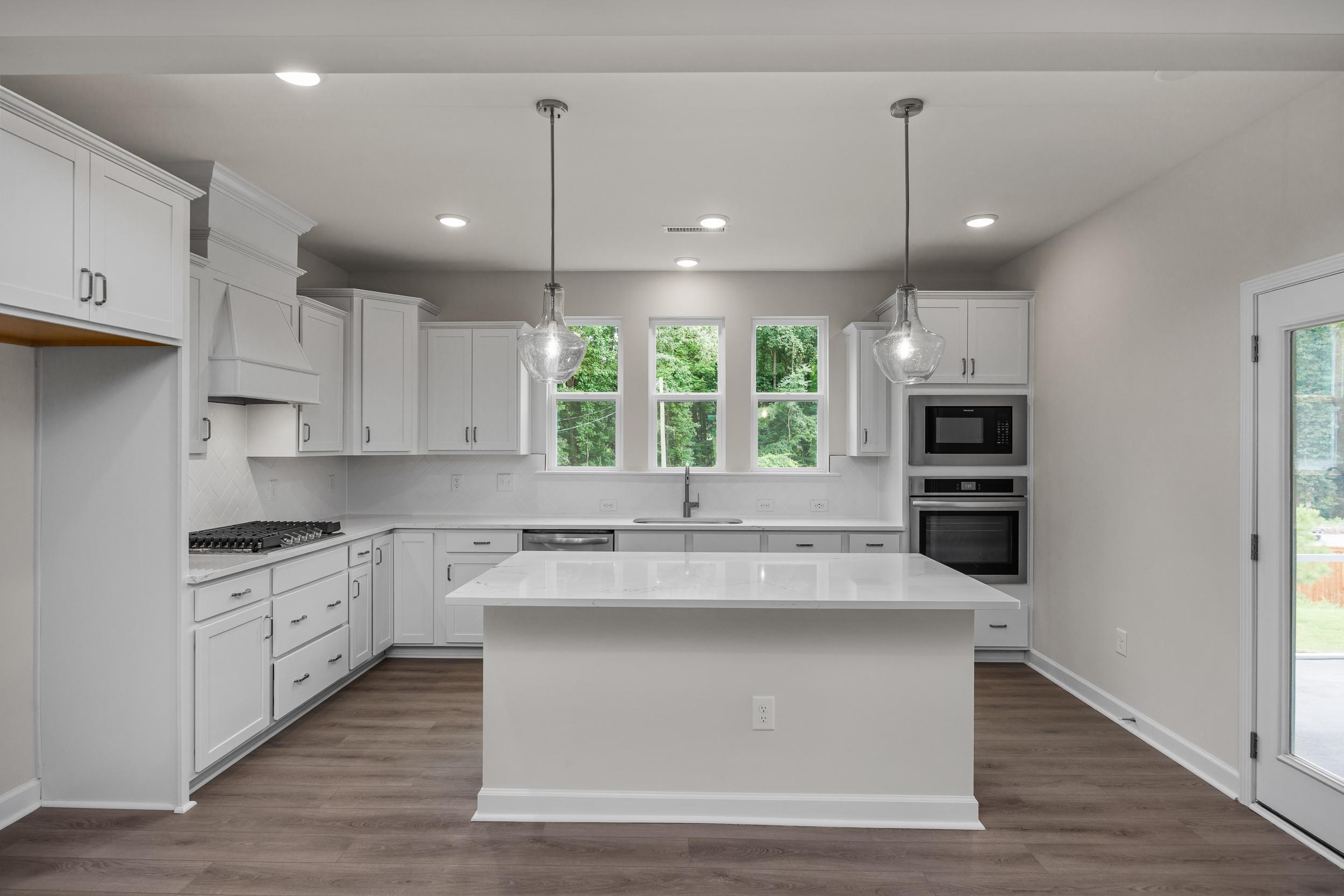 Modern white kitchen in The Aspen Davidson Homes with large quartz island, double ovens, and French doors to patio