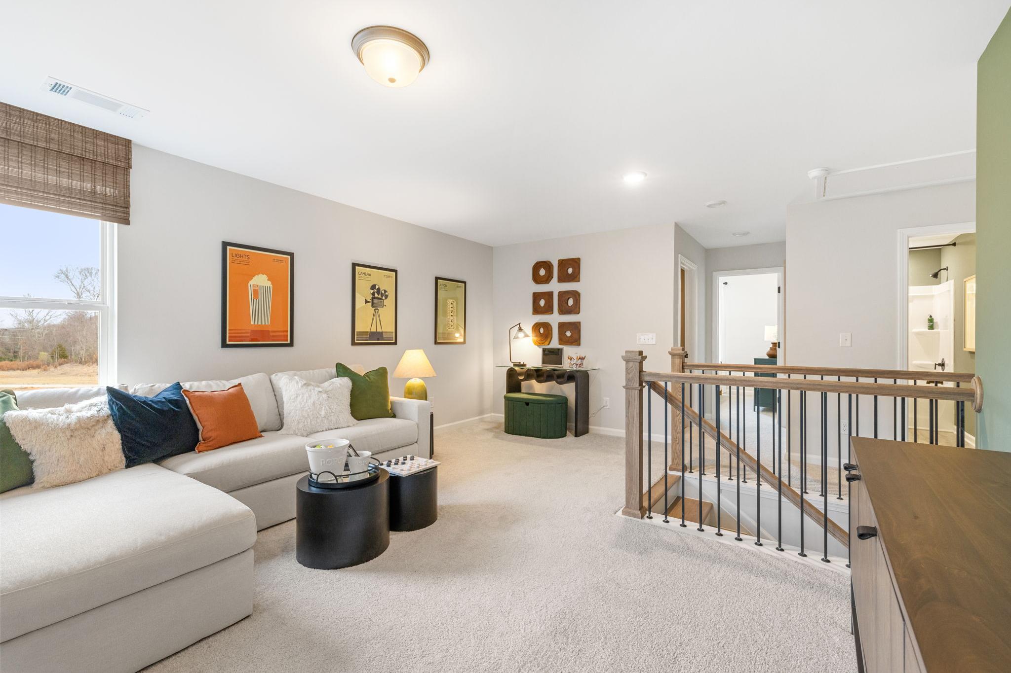 Cozy loft living area in Links Crossing Auburn AL home with L-shaped sofa, colorful pillows, modern artwork, desk, and wooden staircase