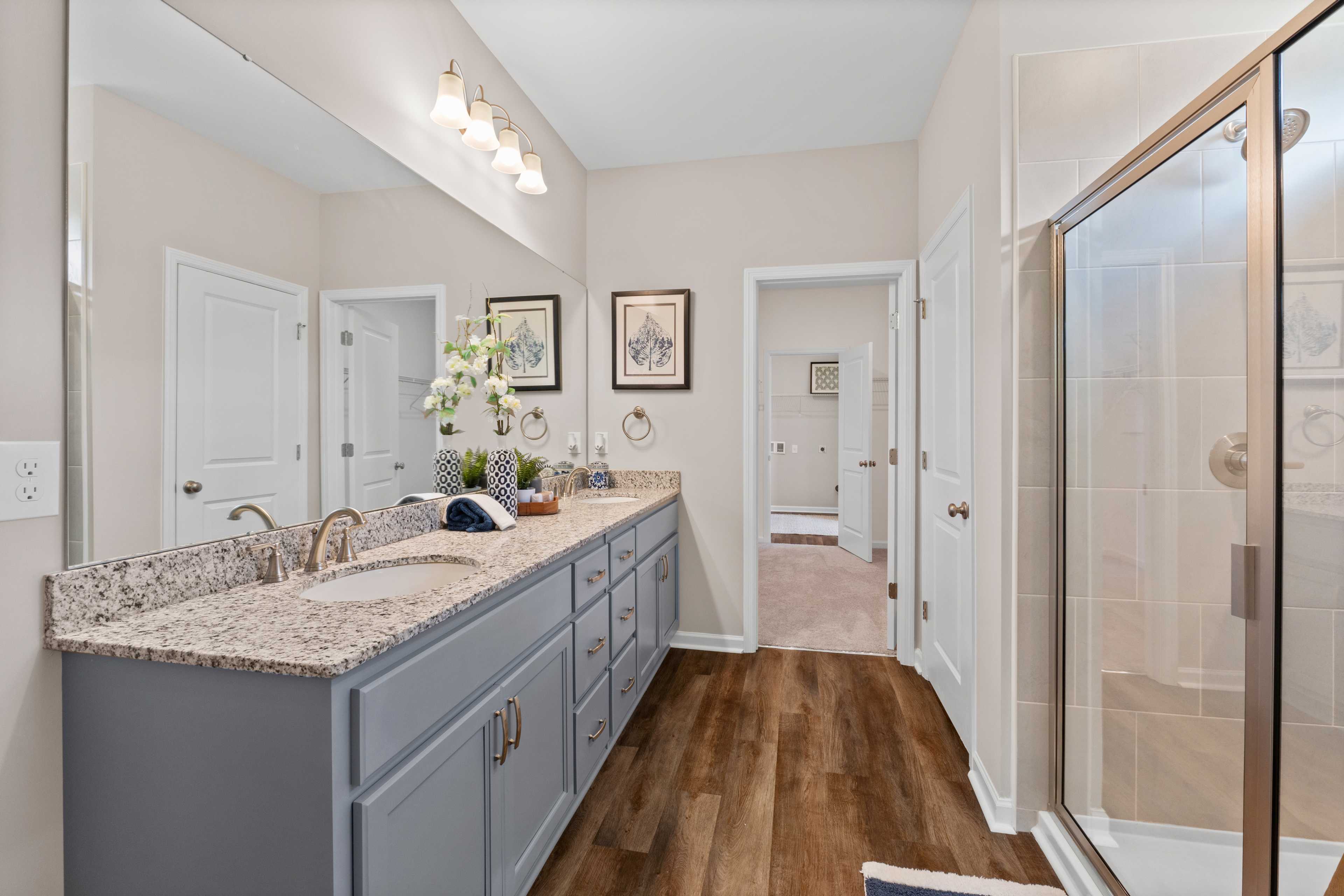 Spacious bathroom at Riverton Preserve in Huntsville Alabama with gray vanity quartz counters wood floors and glass shower