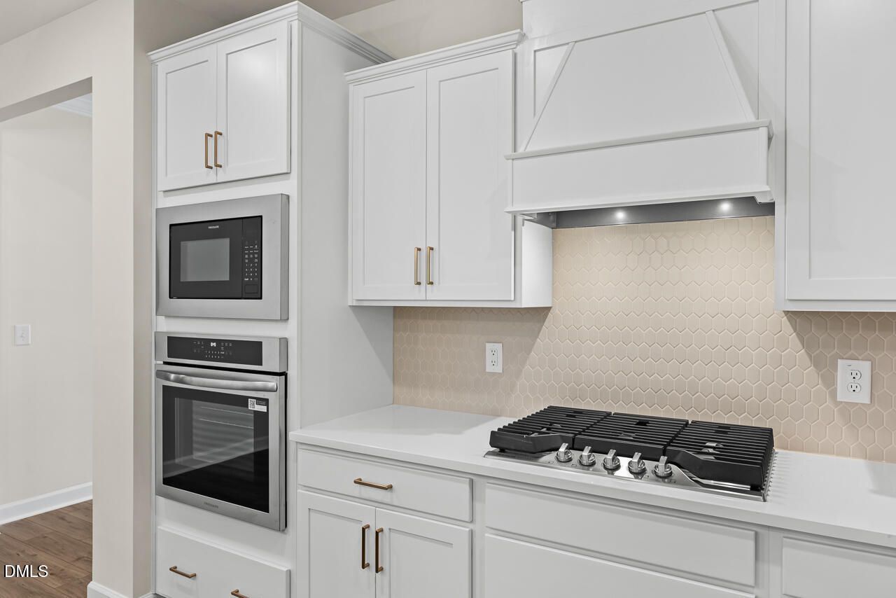 White shaker kitchen with gas cooktop, hexagon tile backsplash, built-in oven and microwave in The Birch II C, Wake Forest NC