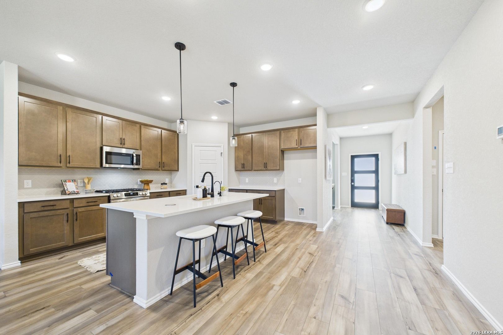 Modern open-concept kitchen with shaker cabinets, white quartz island, bar stools, stainless appliances in The Douglas E, Bricewood, San Antonio