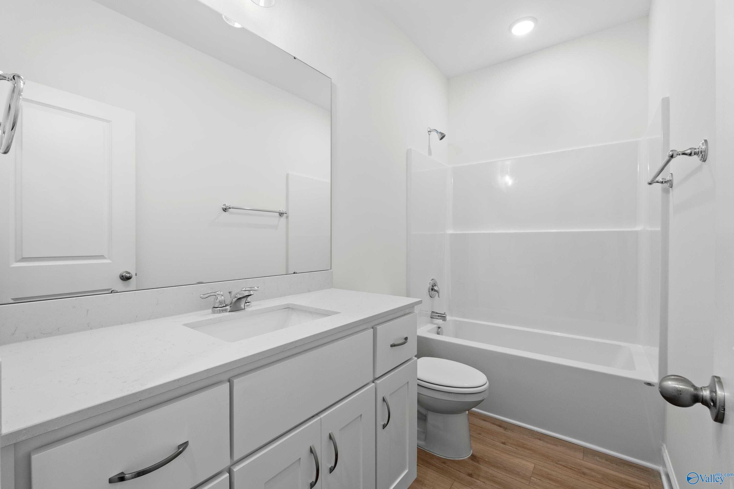 Bright white bathroom with single vanity sink, bathtub shower combo, and toilet in Davidson Homes The Asheville C, Athens Alabama