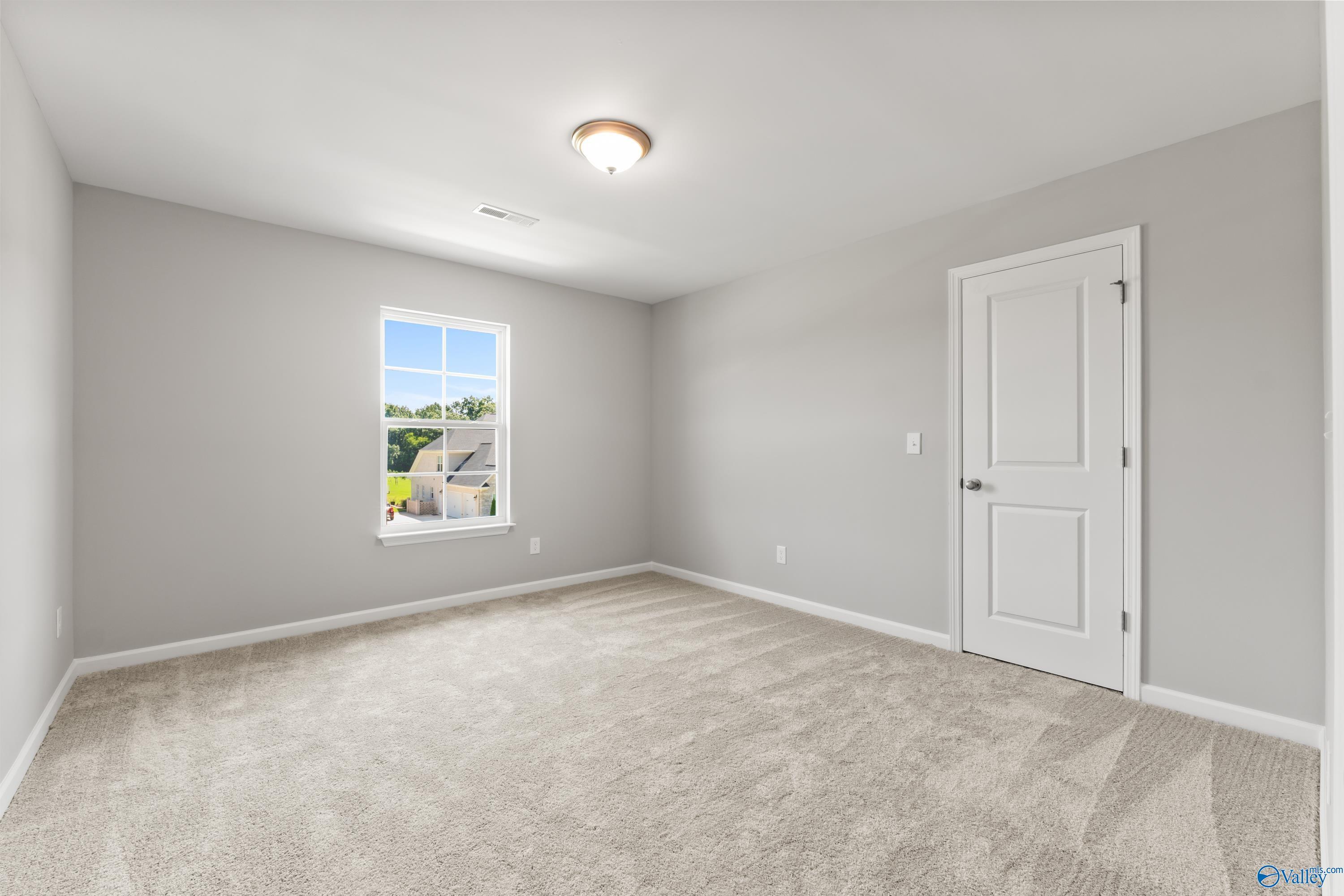 Bright secondary bedroom with light gray walls, beige carpet, and window view in The Charm floor plan, Huntsville, Alabama