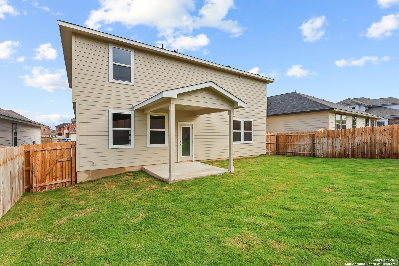 Two-story beige home with covered back patio, glass door, windows, lush green backyard, and wooden fence in Royal Crest, San Antonio, Texas by Davidson Homes The Douglas G