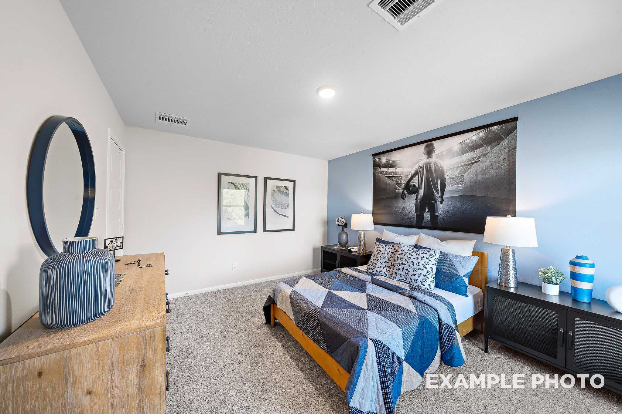 Spacious secondary bedroom in The San Marcos B featuring blue walls, geometric quilt bed, wooden dresser, and modern artwork