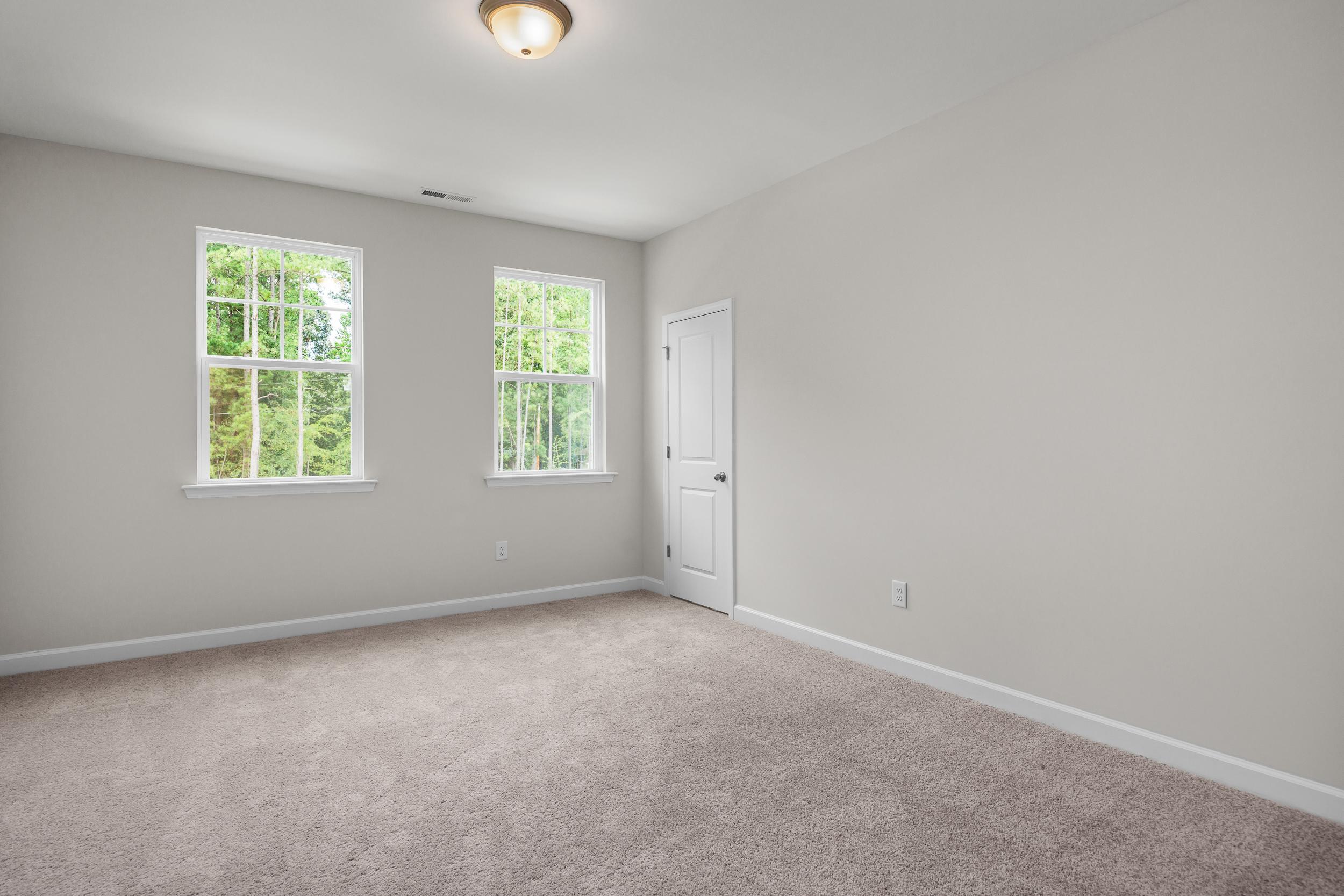 Spacious upstairs bedroom in The Aspen home featuring large windows, light gray walls, white trim, and carpeted floor