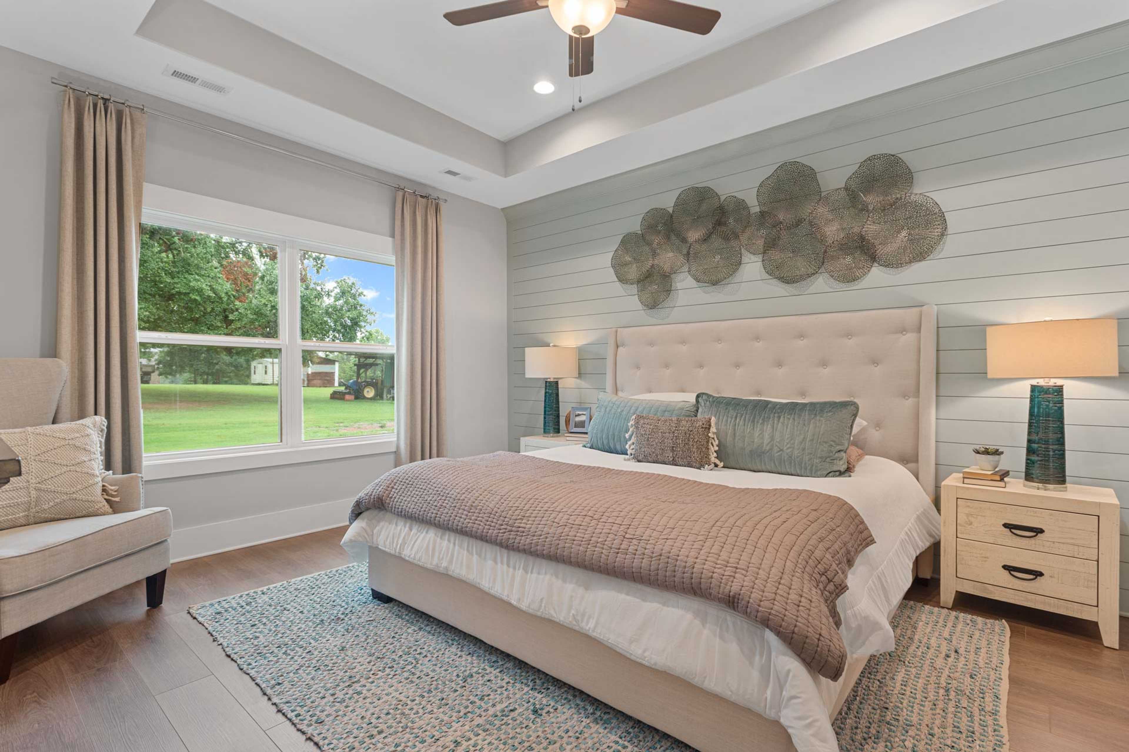 Spacious primary bedroom at Monteagle Cove in Owens Cross Roads AL with tufted beige bed, shiplap wall, ceiling fan, and large windows