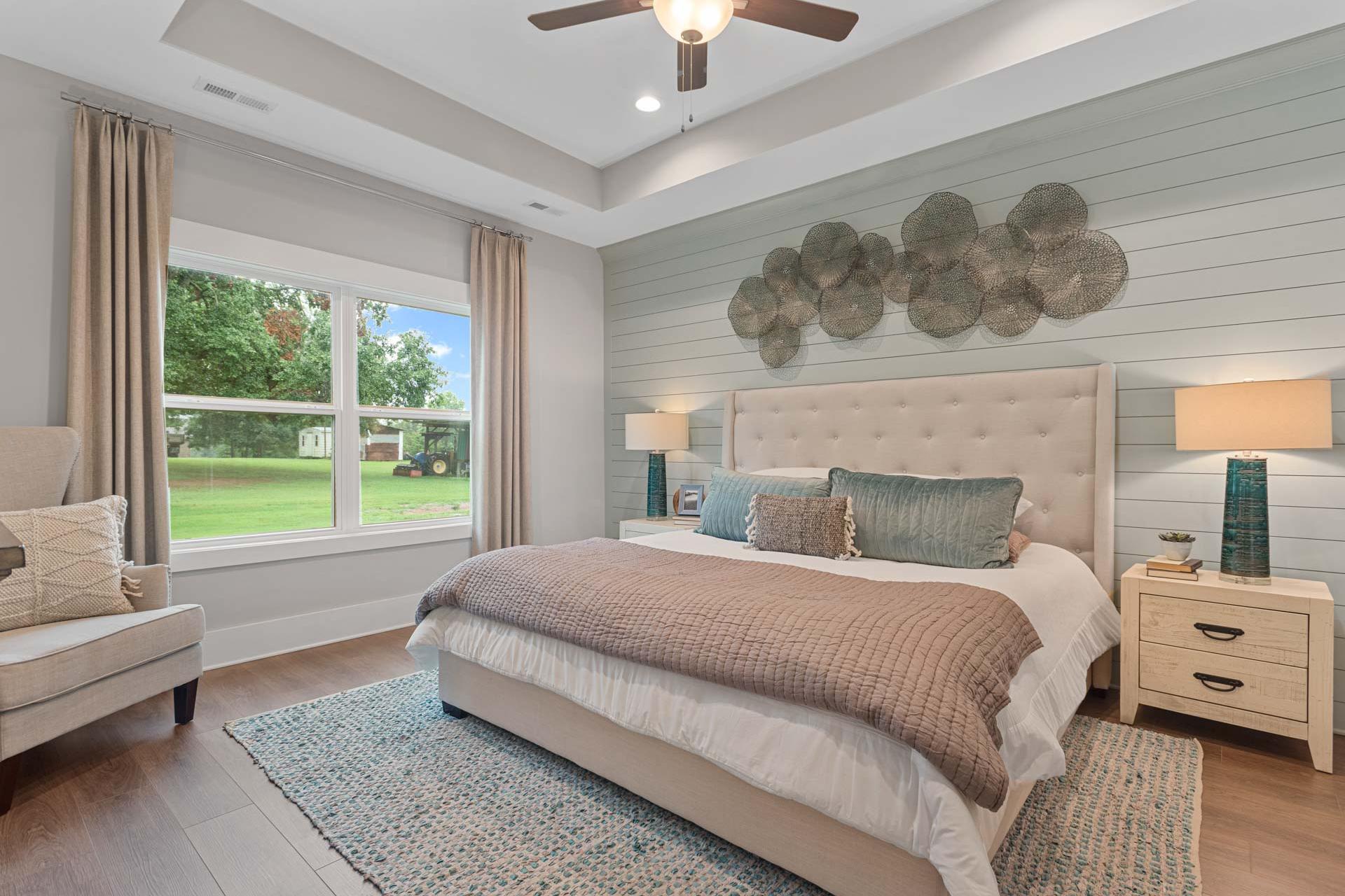 Spacious primary bedroom at Monteagle Cove in Owens Cross Roads AL with tufted beige bed, shiplap wall, ceiling fan, and large windows
