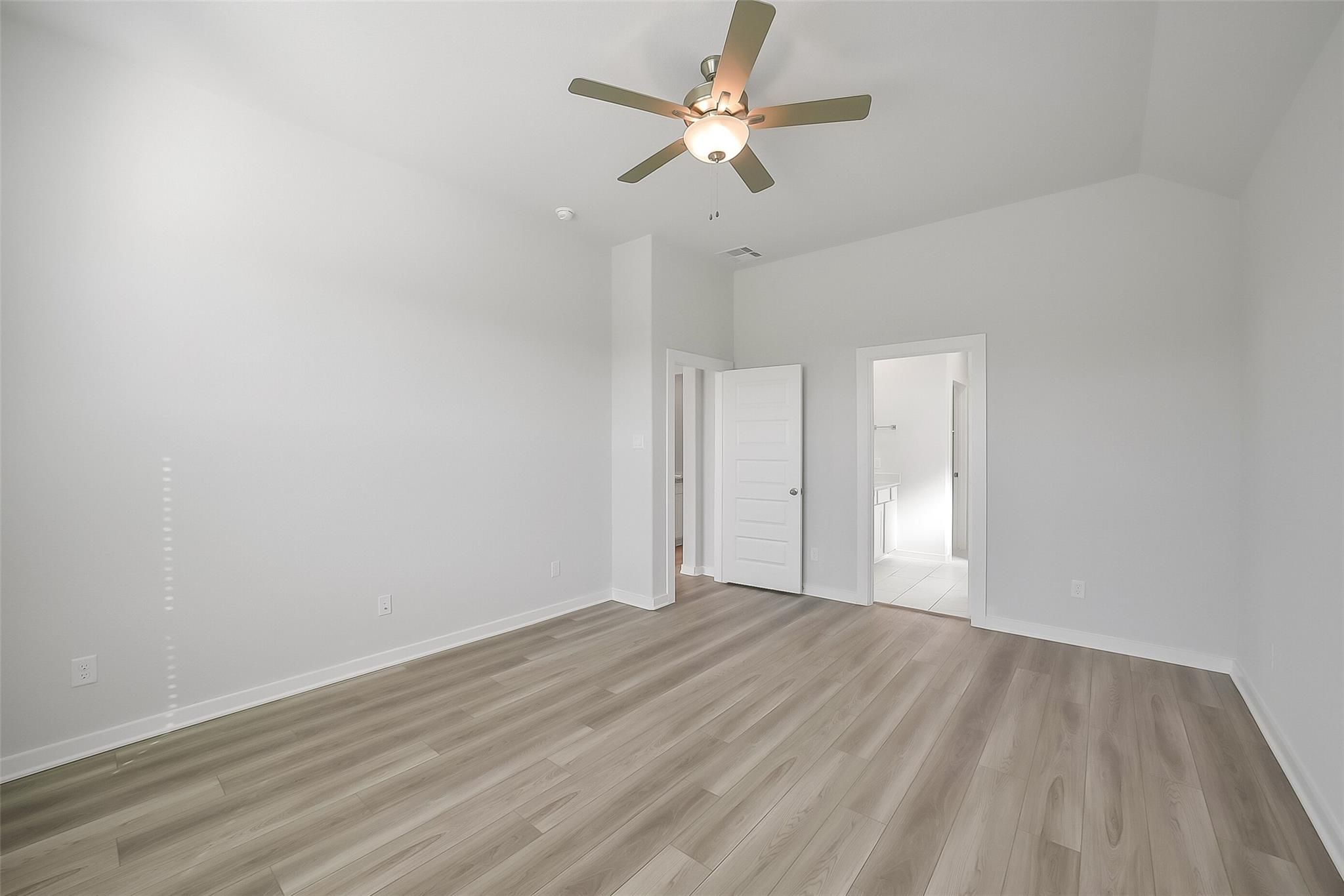 Spacious bedroom with ceiling fan, en-suite bath door, and laminate flooring in Davidson Homes The Acadia A, Katy, Texas