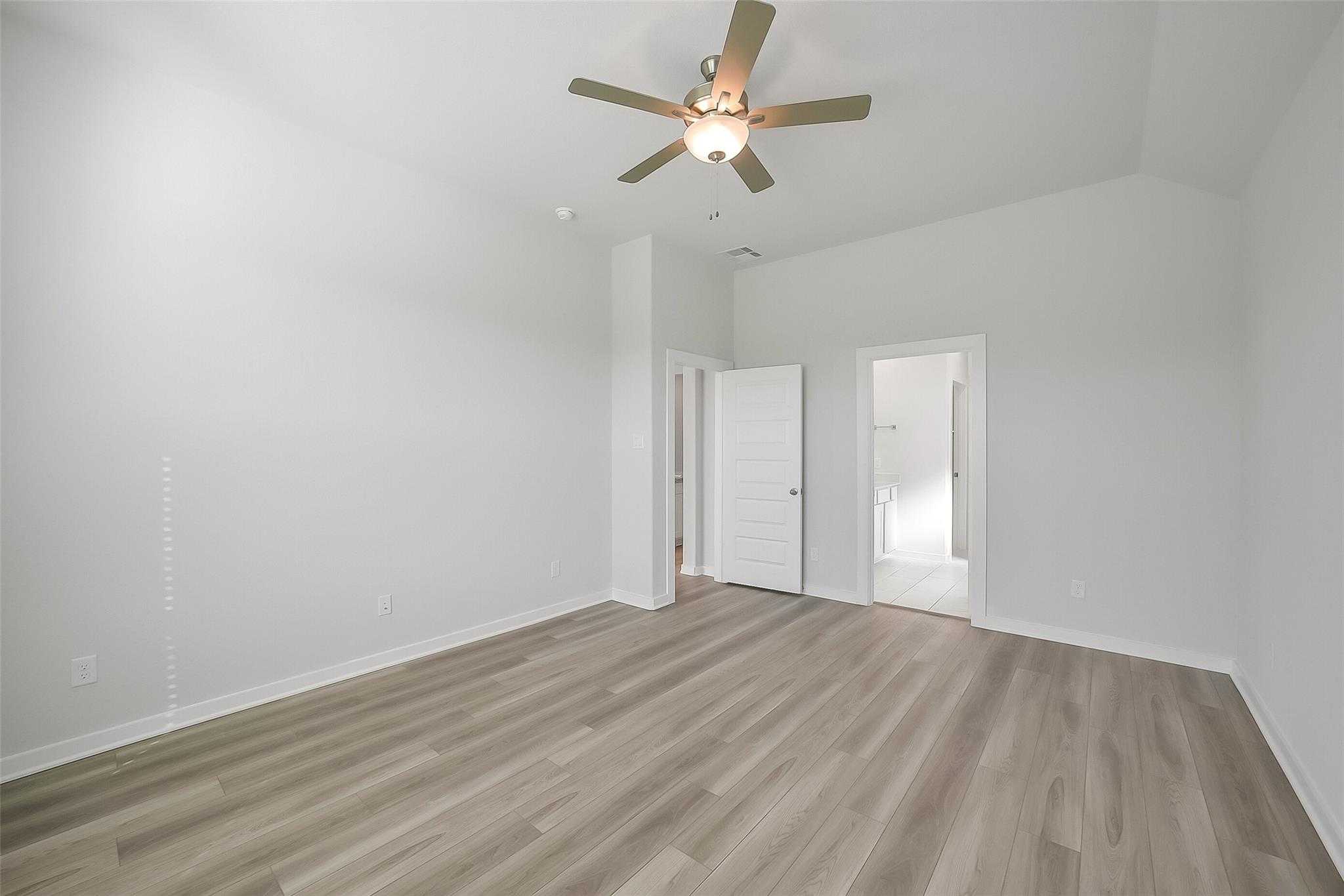 Spacious bedroom with ceiling fan, en-suite bath door, and laminate flooring in Davidson Homes The Acadia A, Katy, Texas