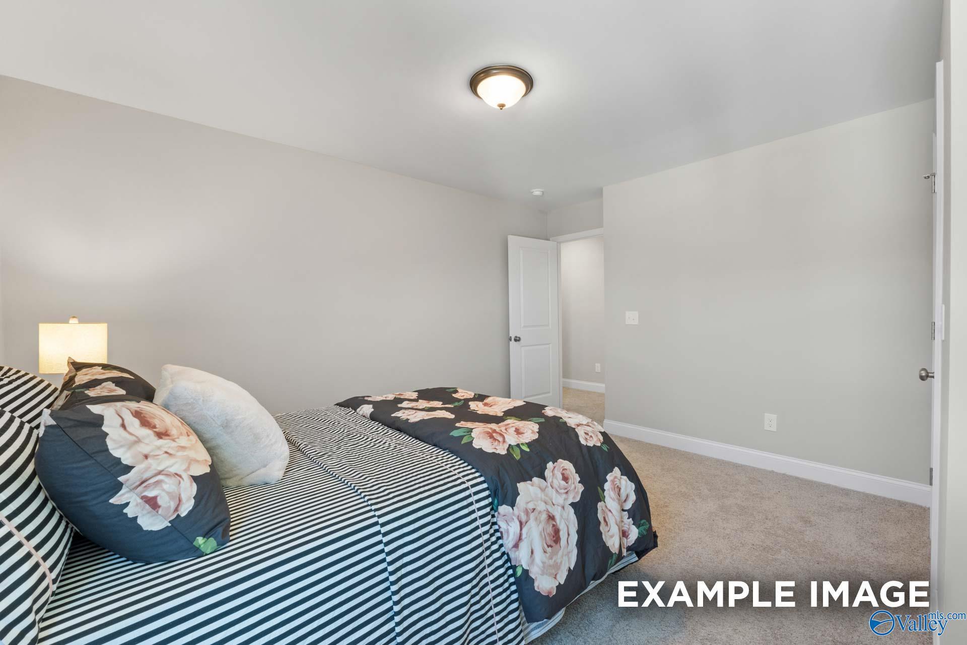 Cozy bedroom with floral rose duvet, striped sheets, and plush pillows in Evermore Homes The Haven E, Owens Cross Roads, Alabama