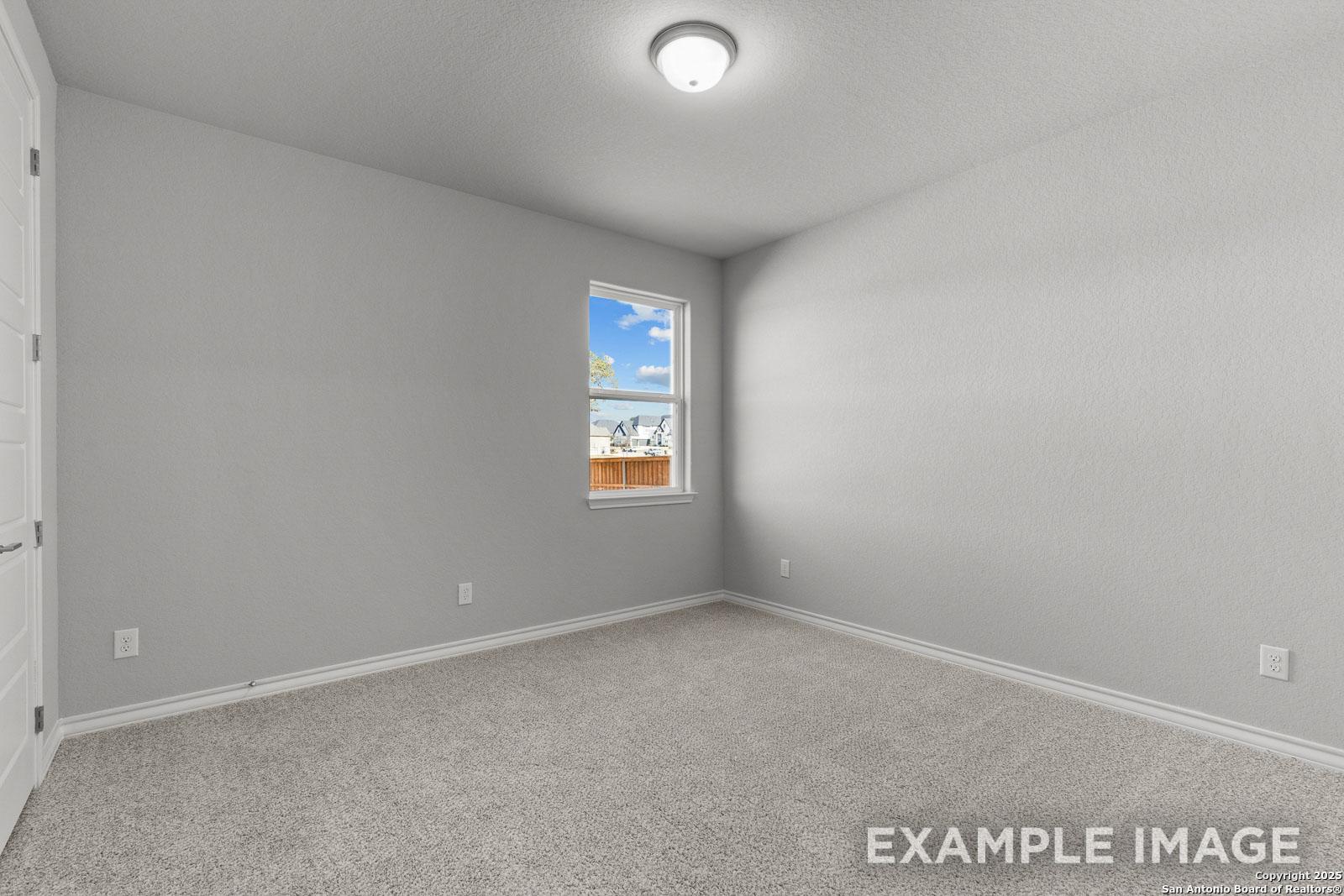 Spacious secondary bedroom in The Oxford H floor plan featuring neutral carpet, light gray walls, and natural light.