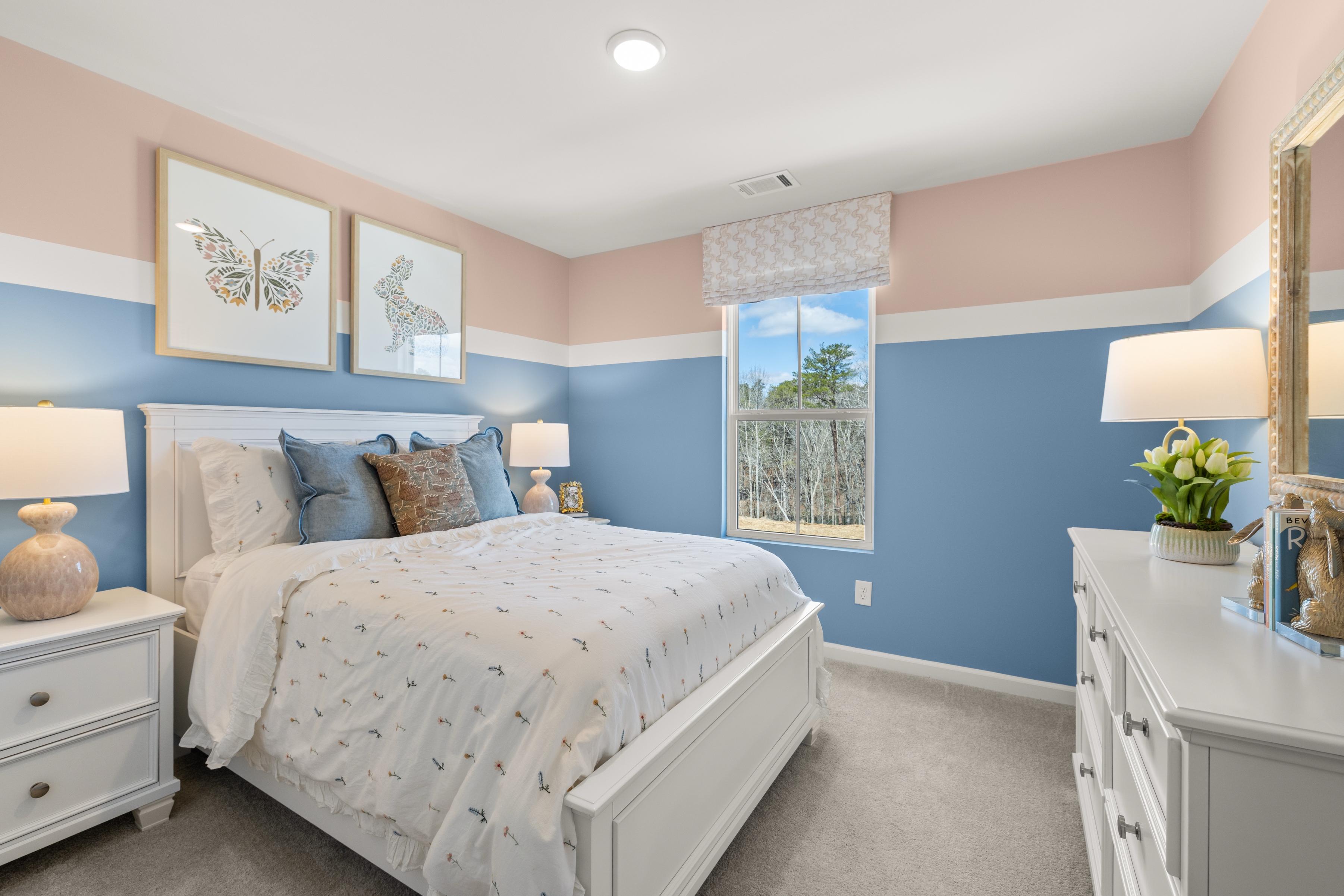 Cozy bedroom at The Bluffs in Canton Georgia with blue-pink walls, white bed, butterfly art, lamps, and tree-view window