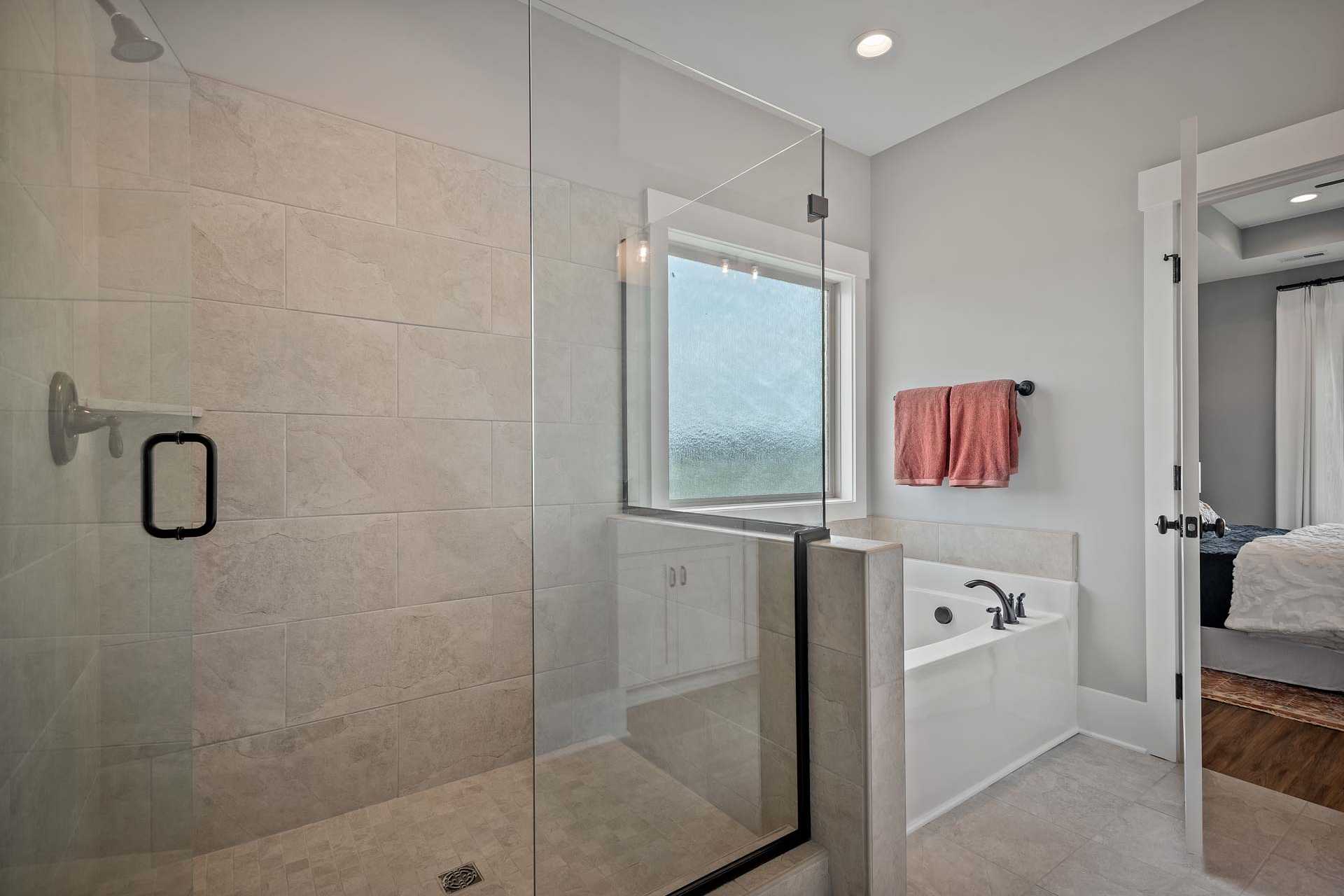 Spacious bathroom at Heritage Lakes in New Market AL featuring frameless glass shower, soaking tub, and beige tile