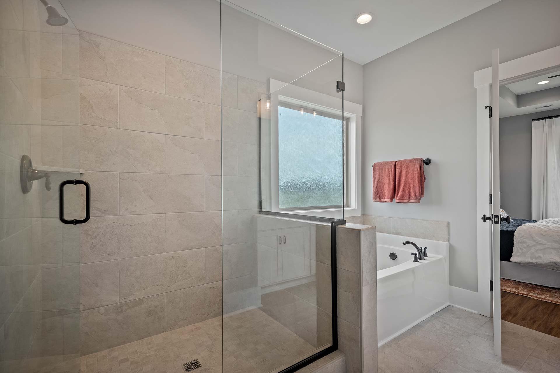 Spacious bathroom at Heritage Lakes in New Market AL featuring frameless glass shower, soaking tub, and beige tile